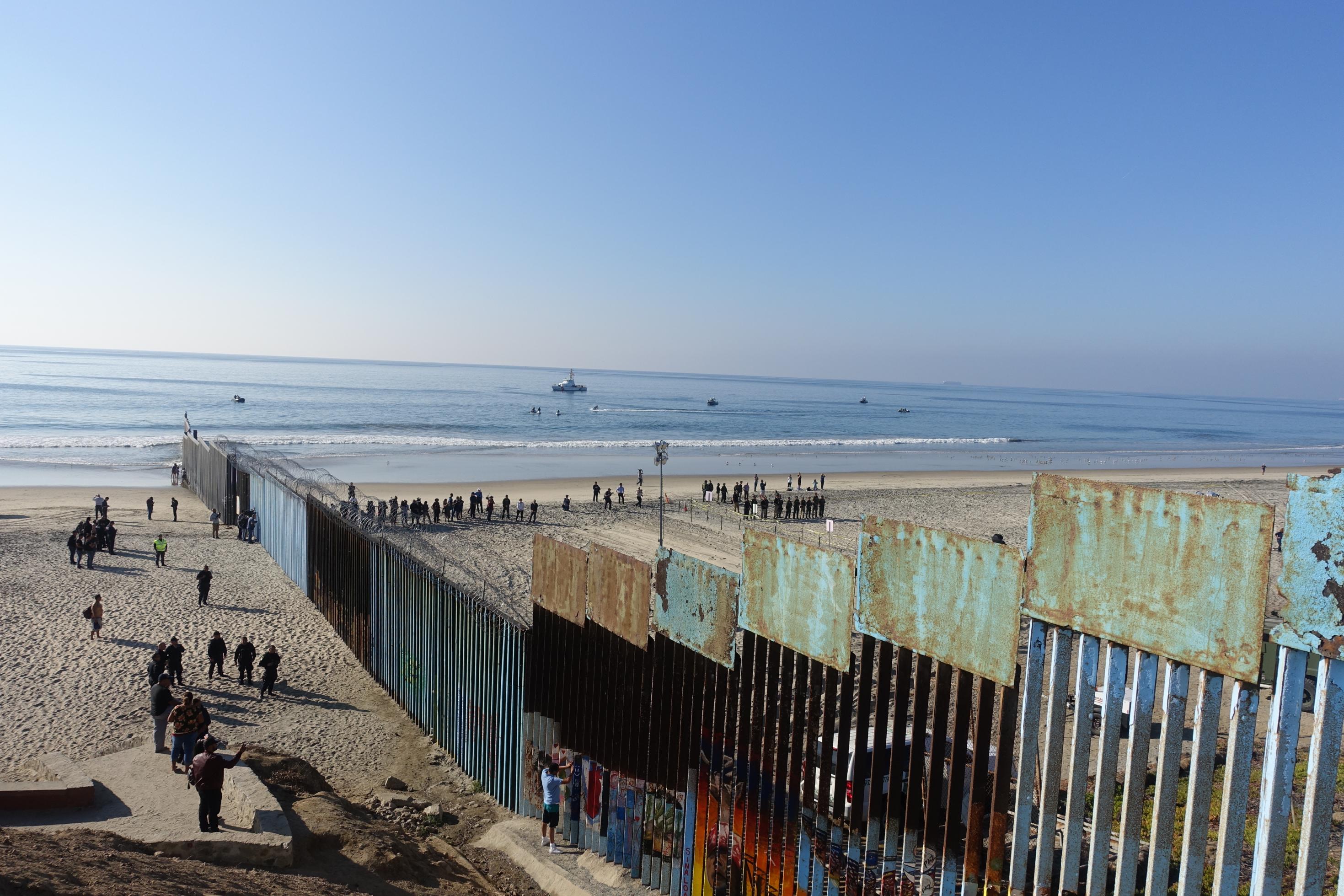 Zu sehen ist ein massiver und sehr hoher Zaun, der über einen Strand bis ins Meer reicht, um ihn möglichst unpassierbar zu machen.