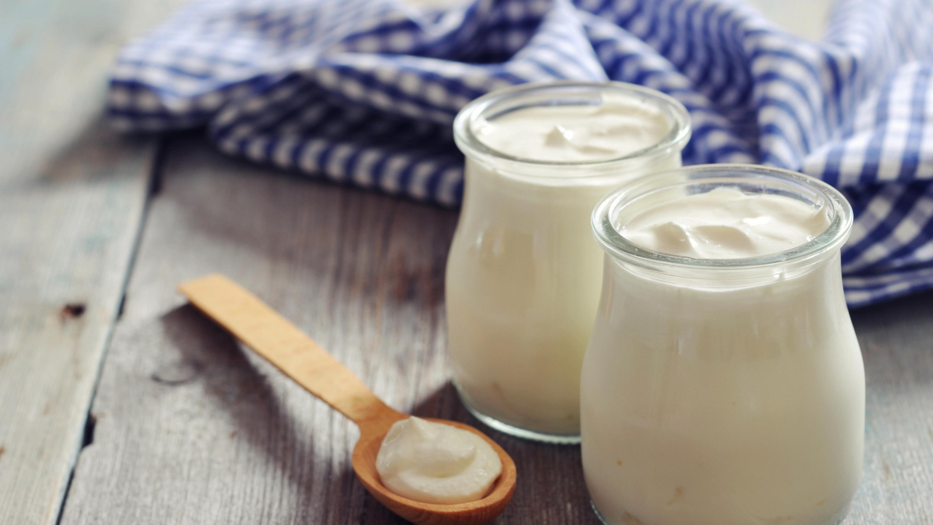 Halbnahe: Zwei Gläser gefüllt mit griechischem Joghurt, davor ein Holzlöffel.