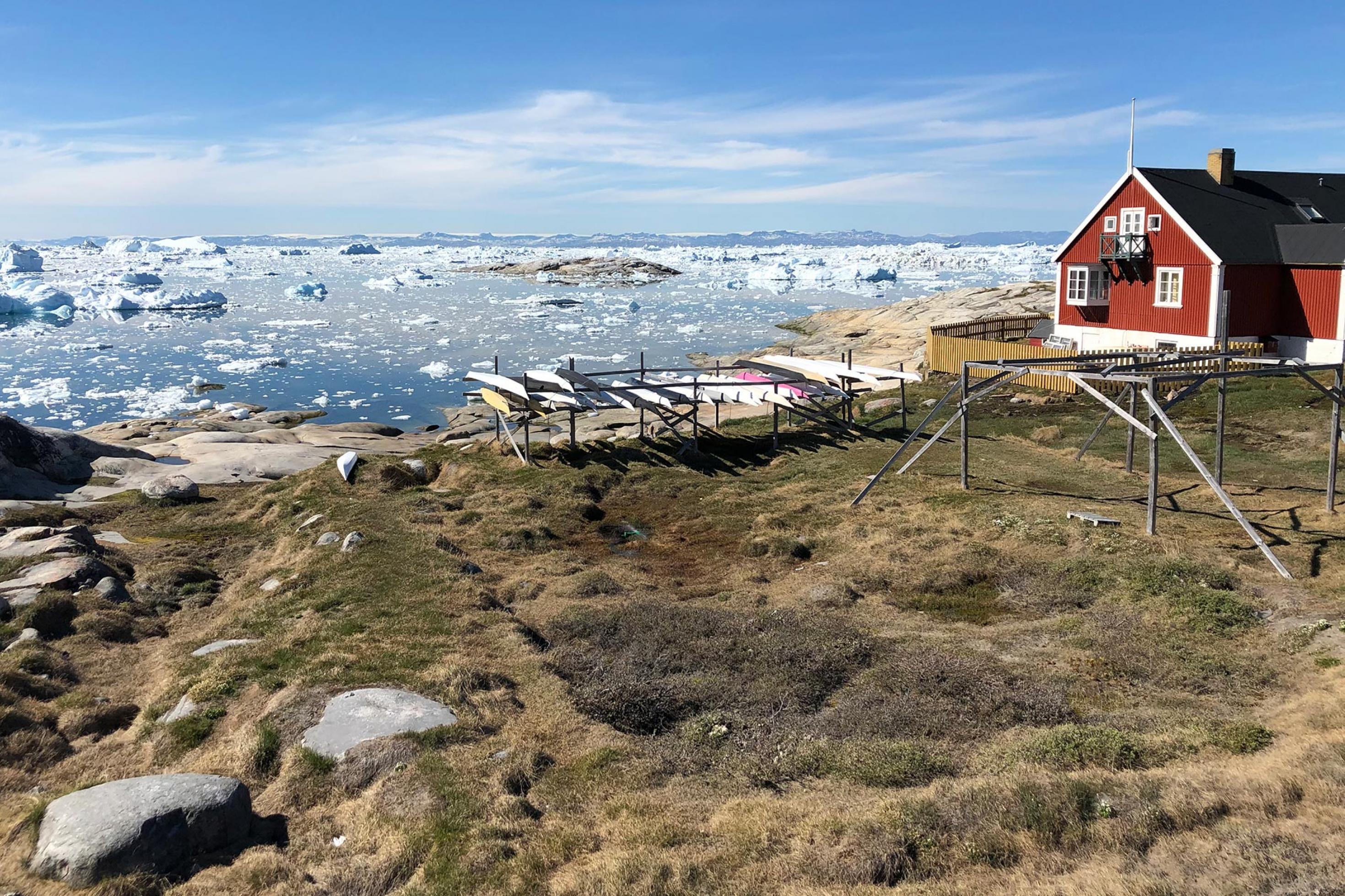 Treibeis vor der arktischen Küste mit einem roten Holzhaus