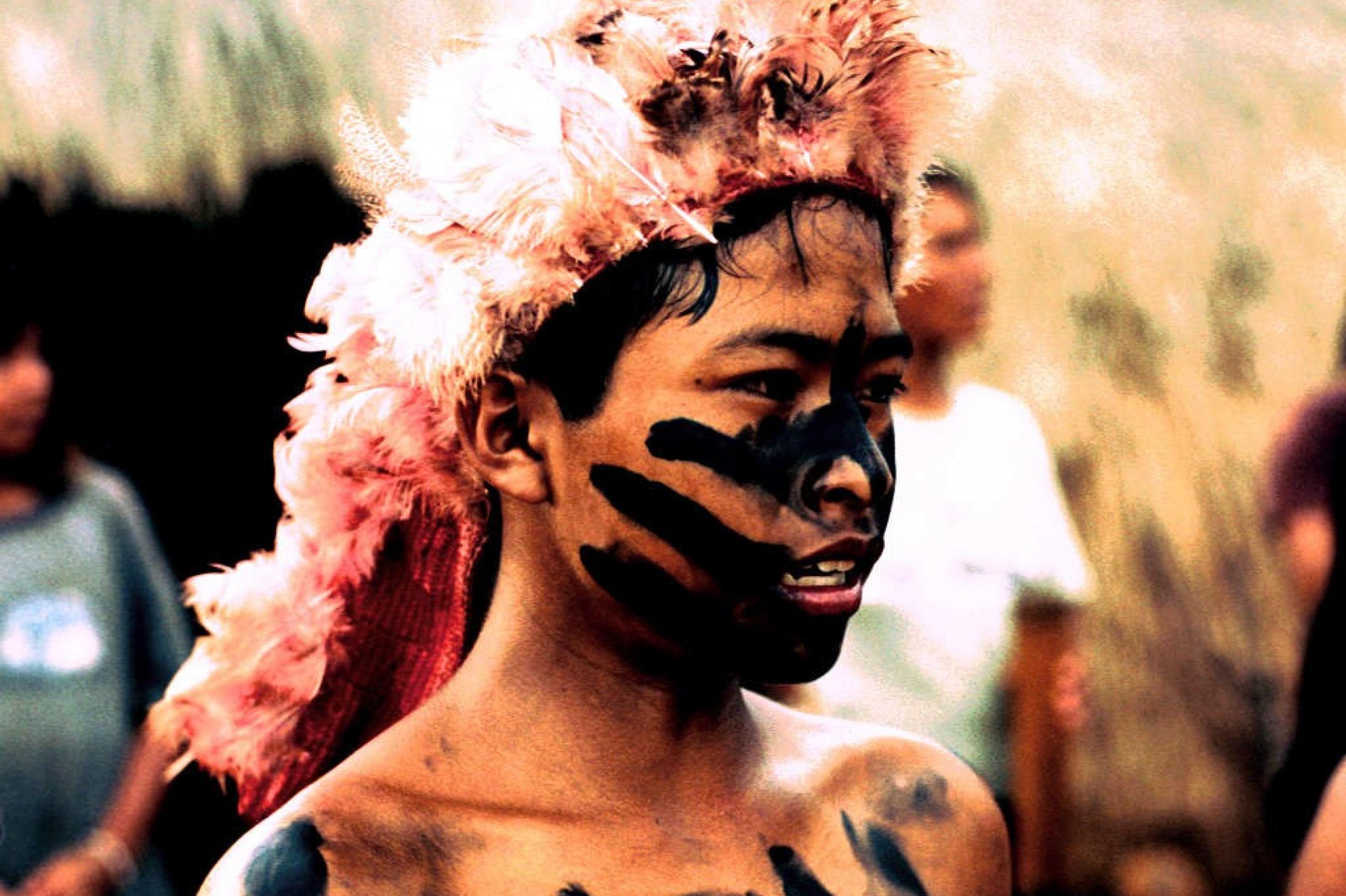 Junger Indigener mit Federschmuck und schwarzer Gesichtsbemalung