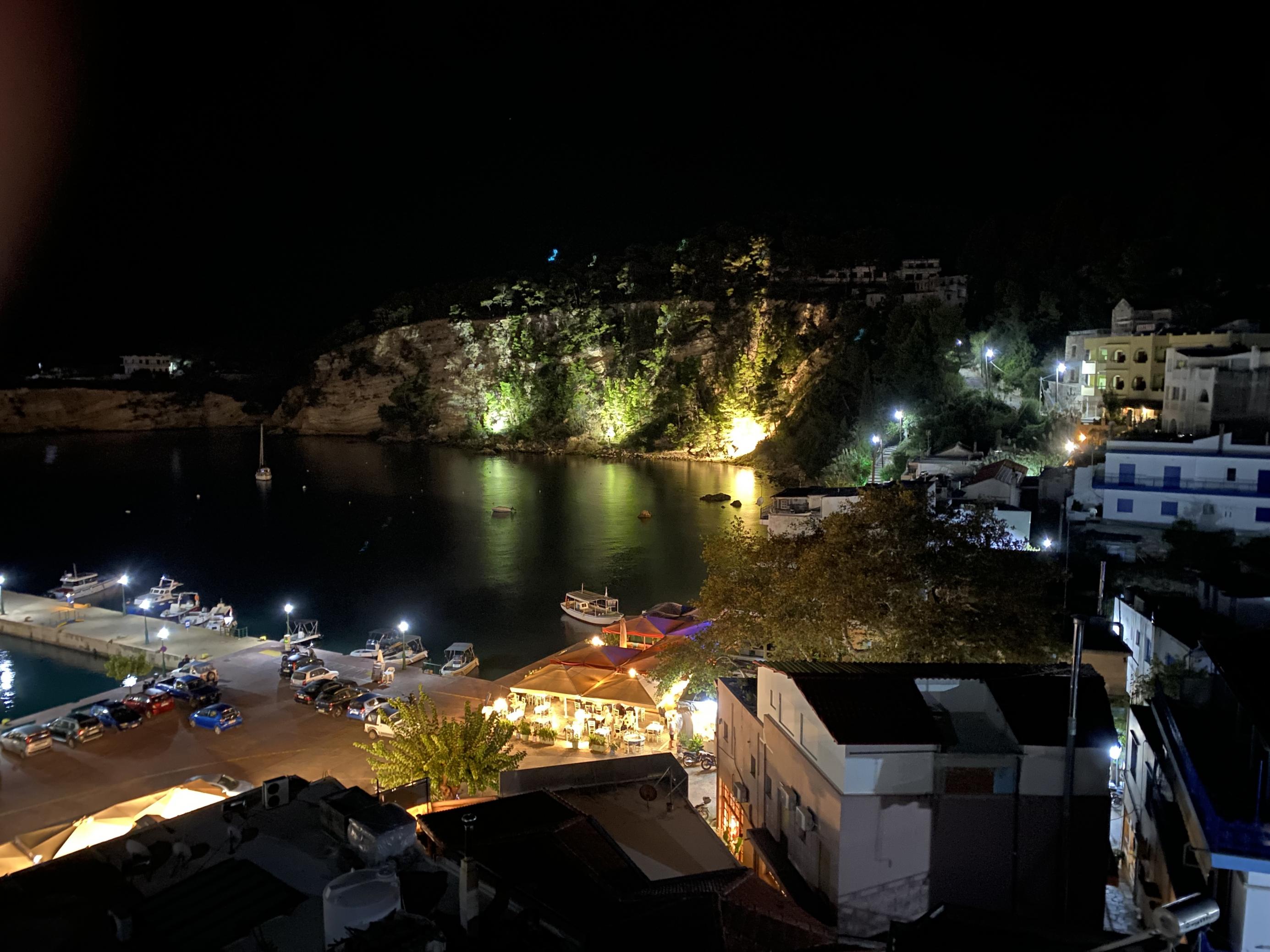 Nächtliche Szene von einem kleinen Hafen mit Strand, Felswand und vielen bunten Lichtern