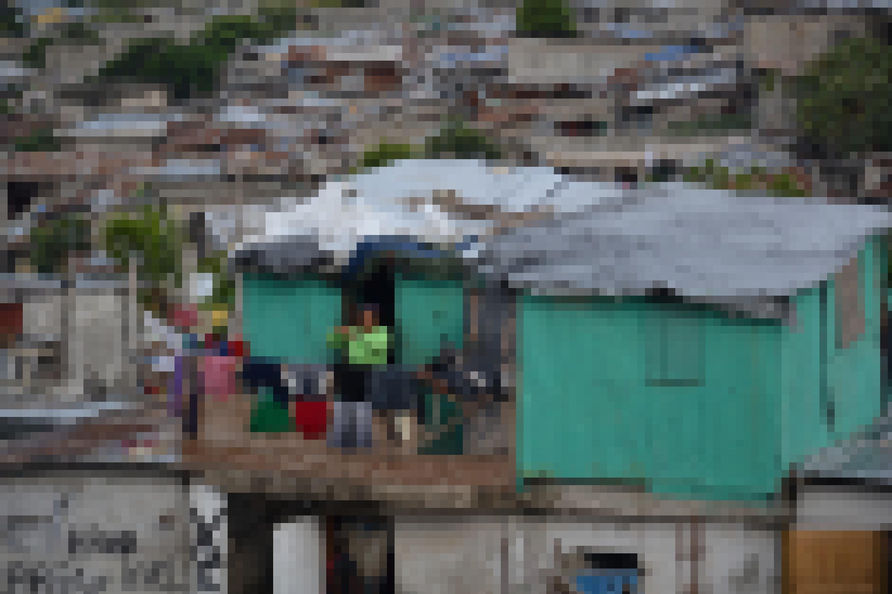 Ein grünes windschiefes Holzhaus, auf dem Balkon kämmt sich eine Frau, dahinter Haitis Hauptstadt in Trümmern.