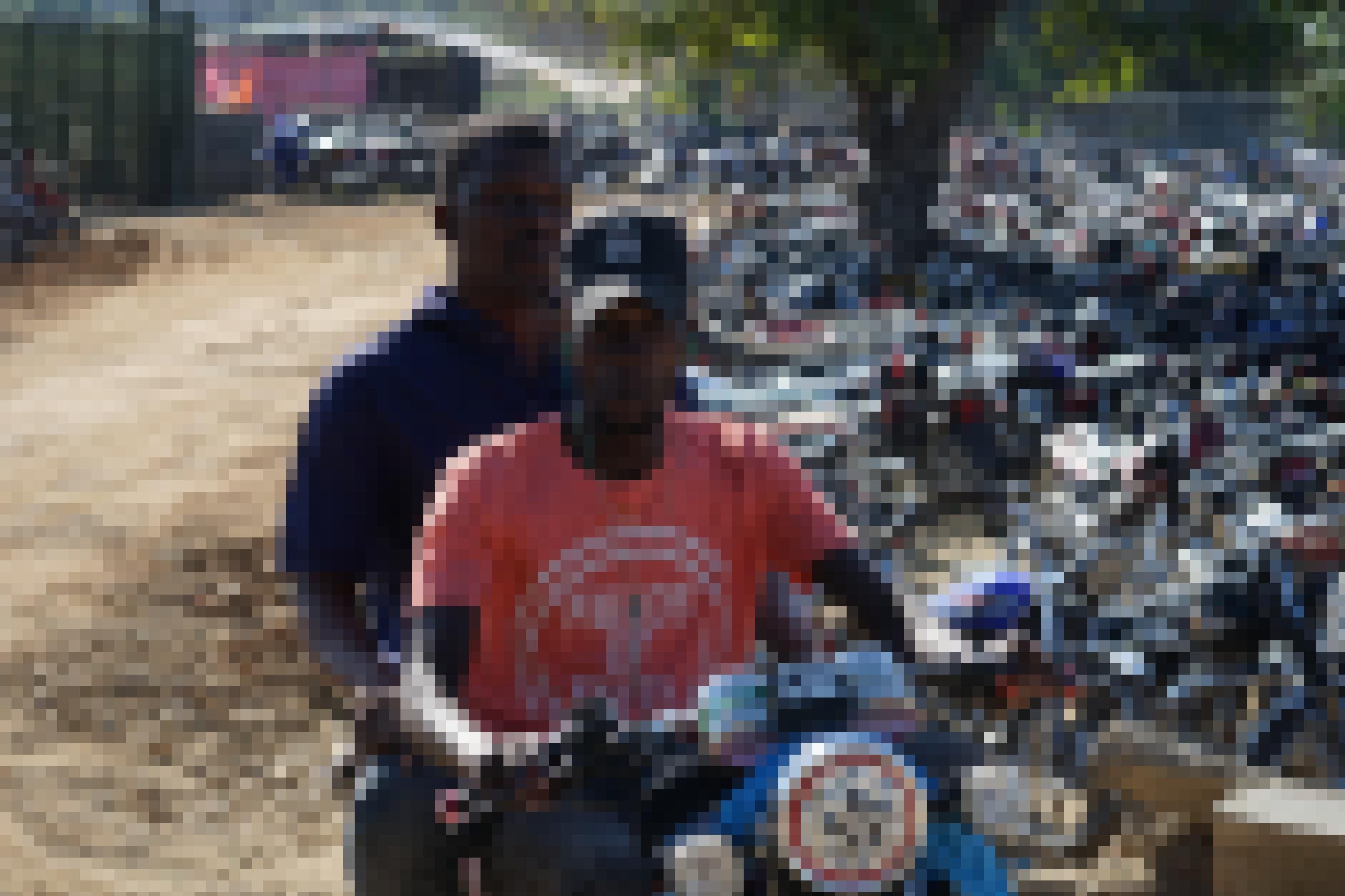 Zwei junge Männer auf einem Motorrad, dahinter hunderte aufgereihter, parkender Mopeds.