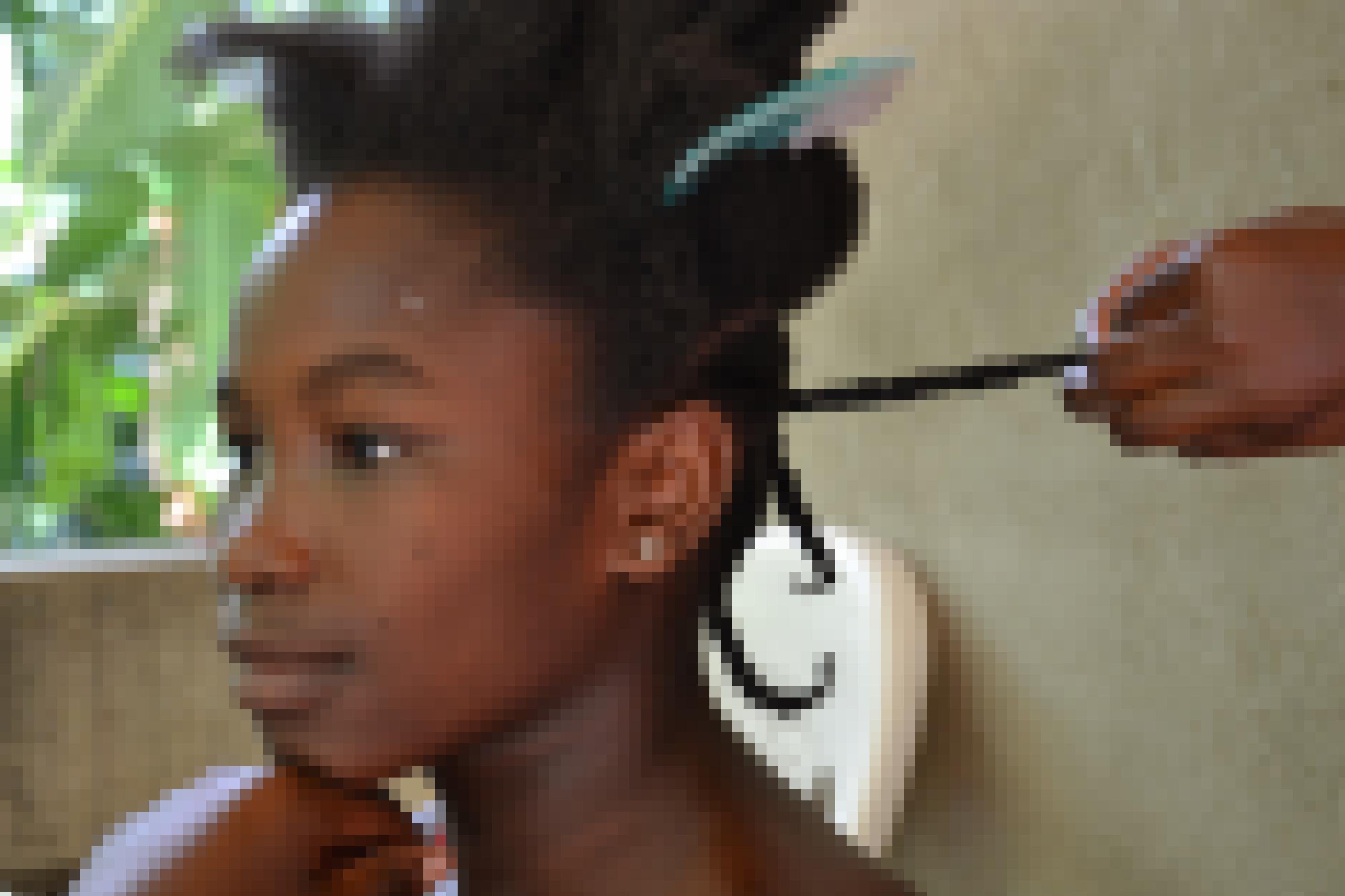 Ein junges Mädchen im Profil mit langen Zöpfen, die gerade geflochten werden.