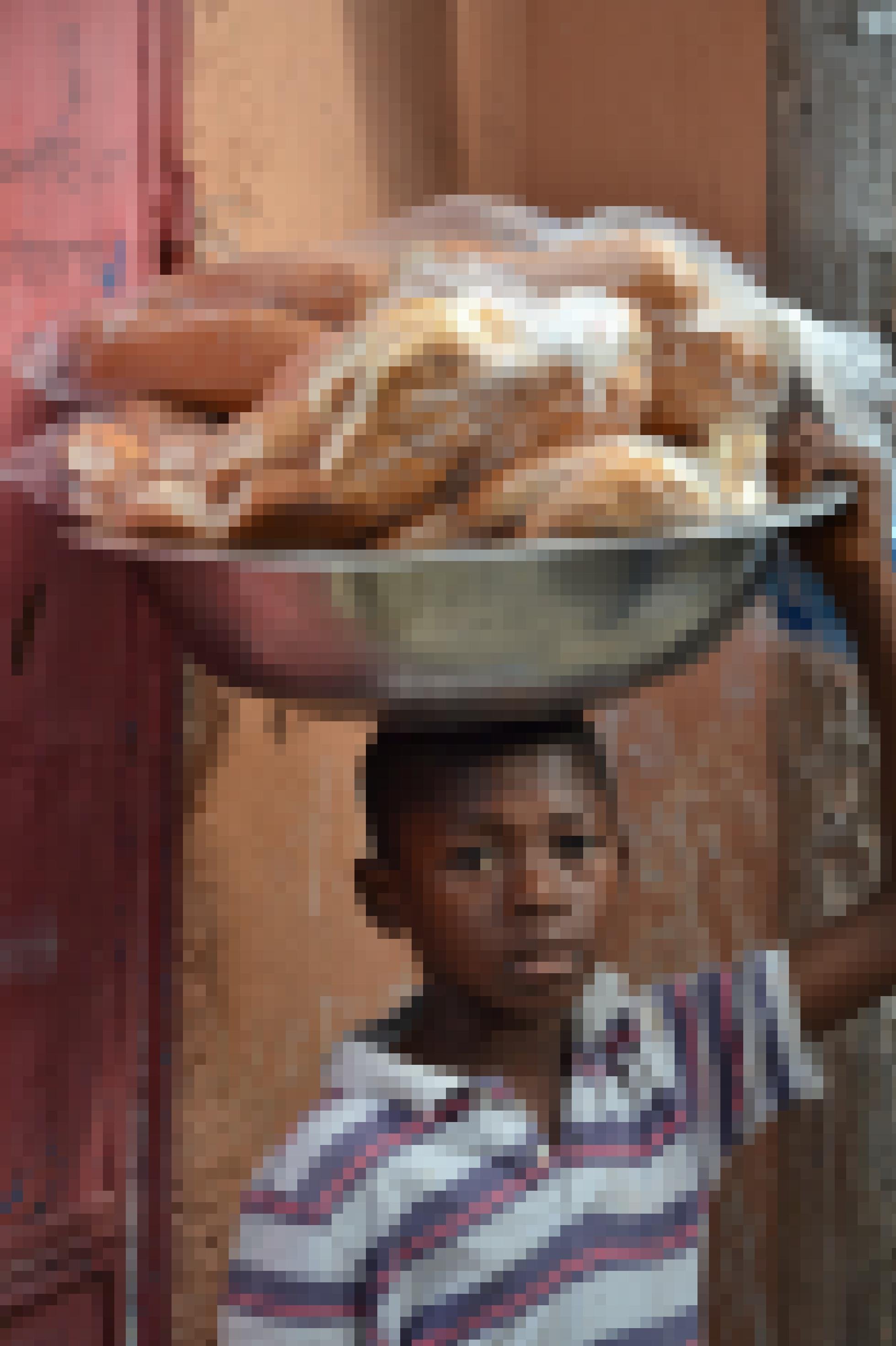 Ein kleiner Junge mit einer grossen Aluschüssel voller Brot auf dem Kopf.
