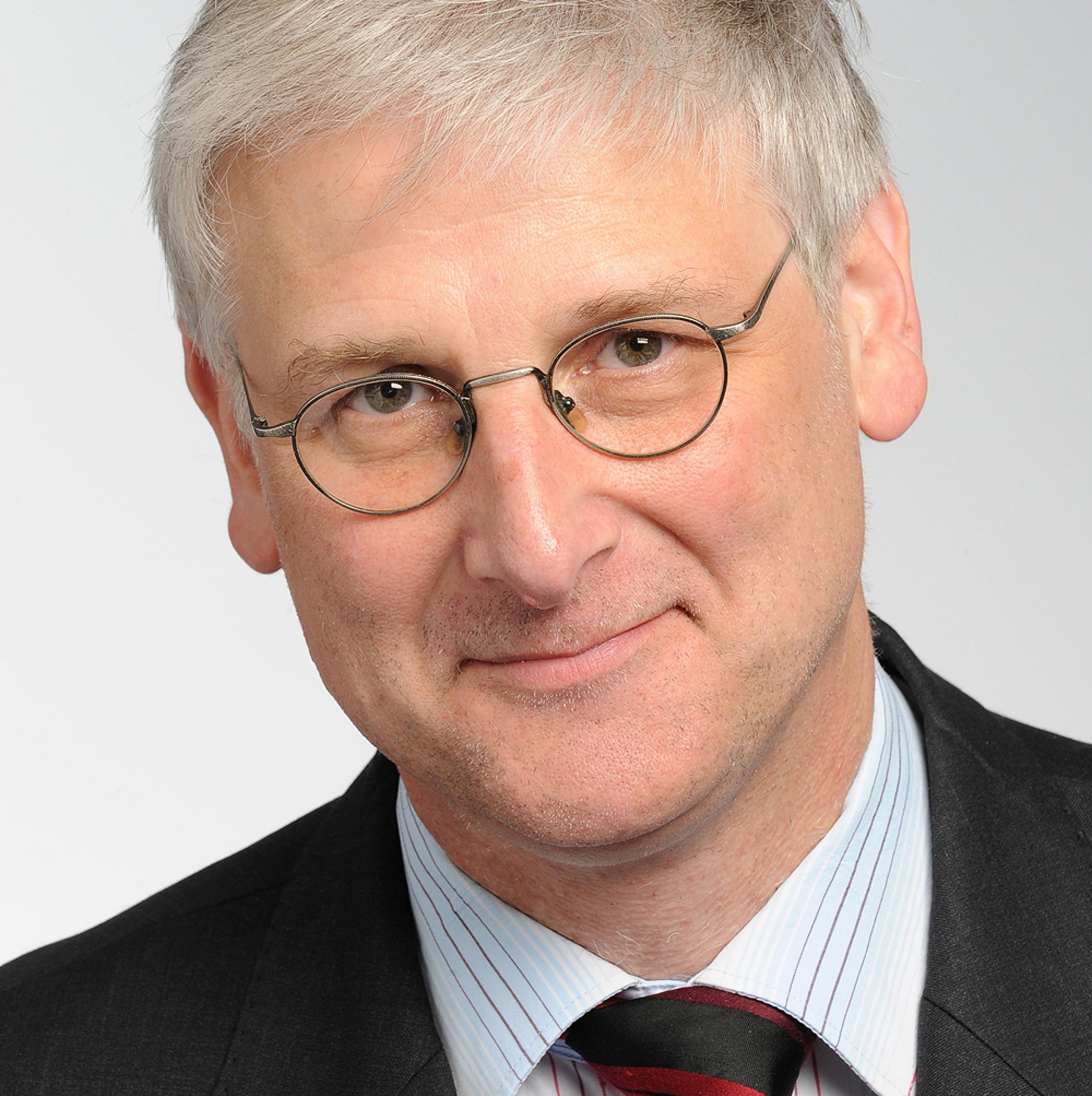 Ein älterer Mann mit Brille und grauen, kurzen Haaren.