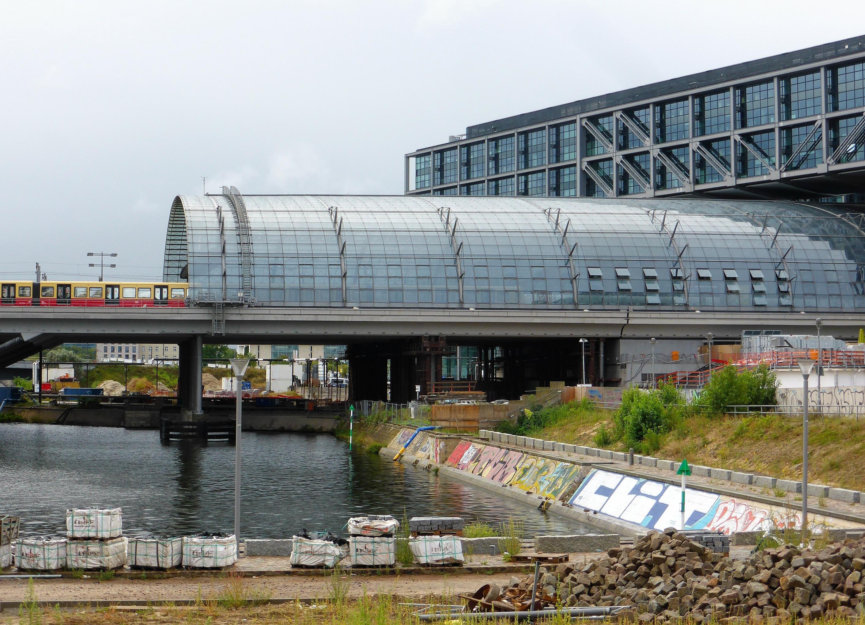 Ostansicht der oberirdischen Gleisausfahrt des Hauptbahnhof Berlin, festgehalten mit einer einfahrenden gelbroten S-Bahn.