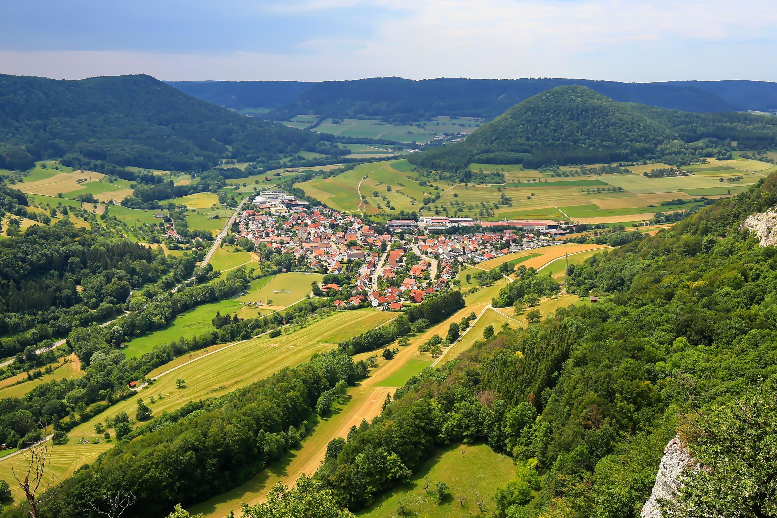 Inmitten leuchtenden Grüns und flankiert von dunklen, bewaldeten Berghängen liegt ein Ort inmitten eines weiten Tales.