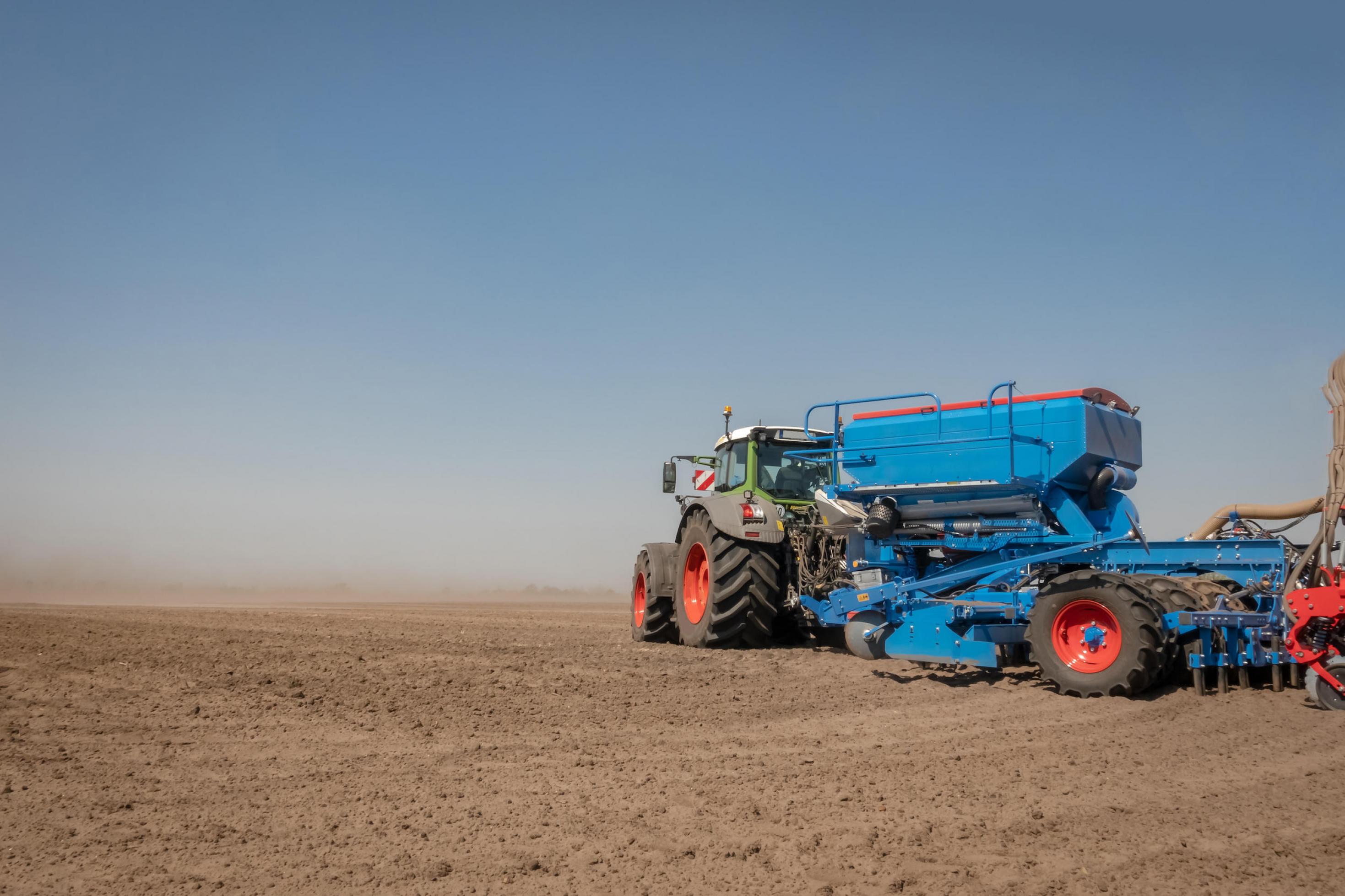 Ein großer Traktor auf einer weiten, staubigen Ackerfläche.