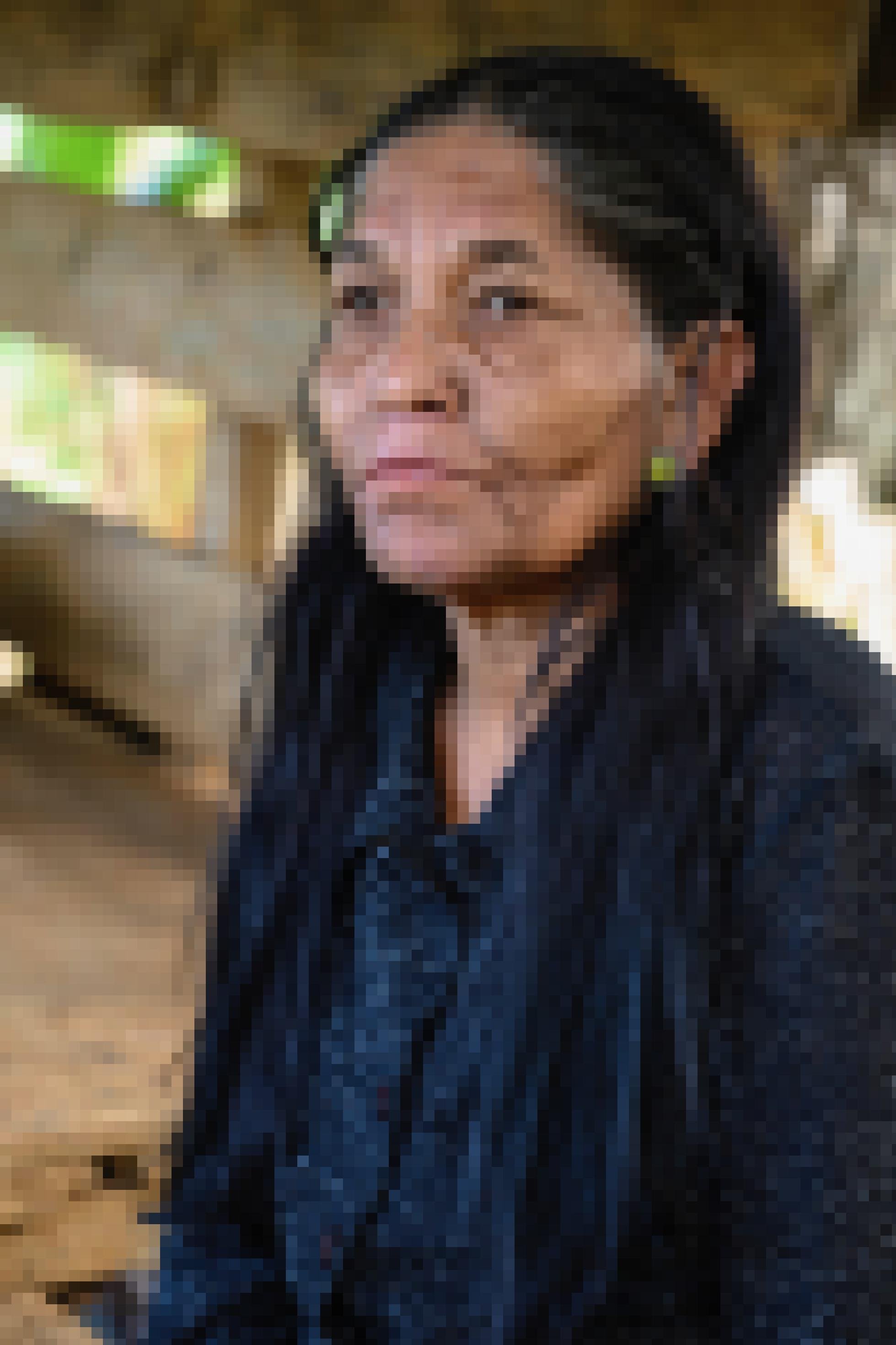 Eine Frau mit langen schwarzen Haaren, den typischen Augenwulsten, mandelförmigen Augen und einer schmalen Nase vor dem Hintergrund ihrer Holzhauses