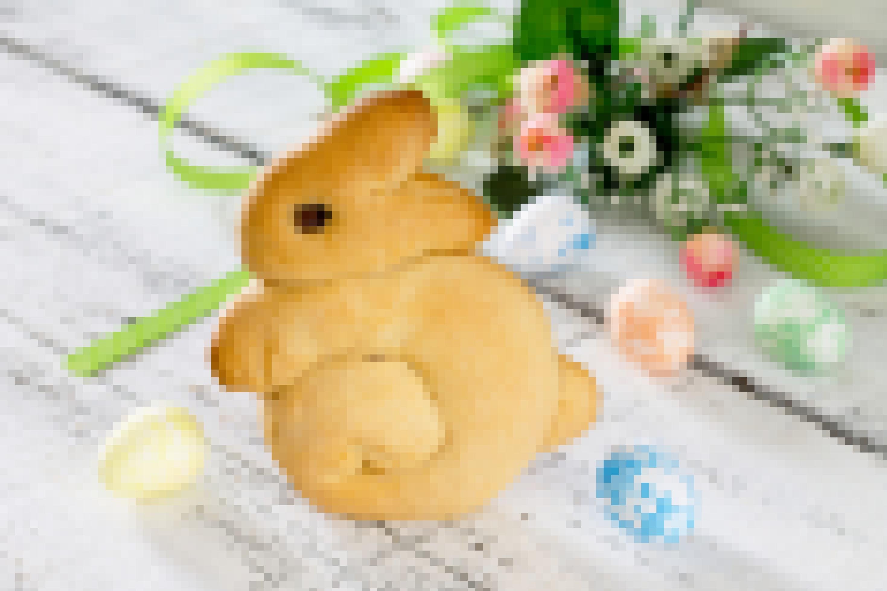 Auf einem weißen hölzernen Tisch steht ein Hase, der aus Hefeteig gebacken wurde. im Hintergrund ein kleiner Frühlingsstrauß und ein paar kleine bunte Eier.