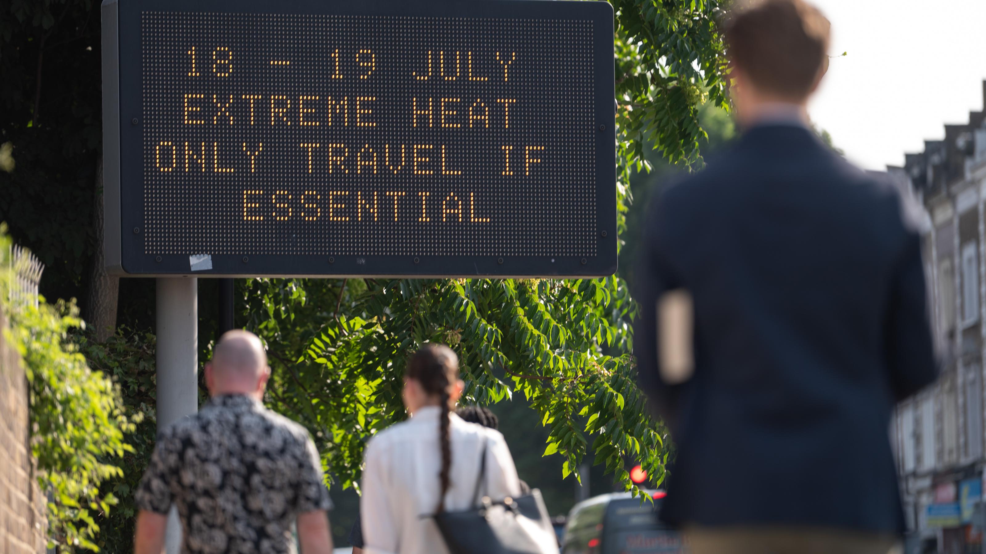 Passanten gehen auf eine LED-Tafel zu. Dort ist der Hinweis zu lesen: „18 –19 July extreme heat only travel if essential“
