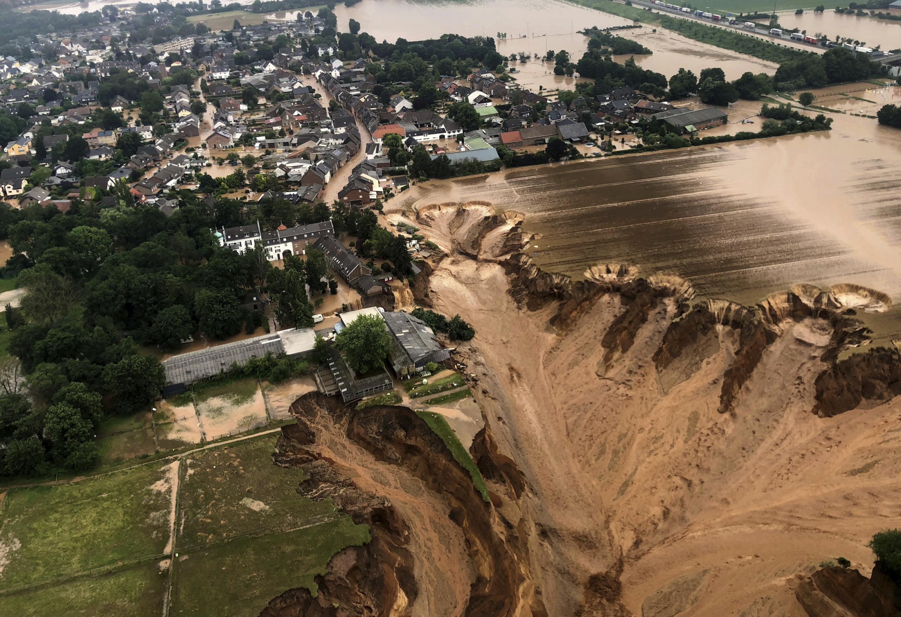 Luftaufnahme von Blessem: Felder und der Rand der Siedlung sind einer großen Abbruchkante gewichen, Wasser fließt hinab in die Sandgrube.