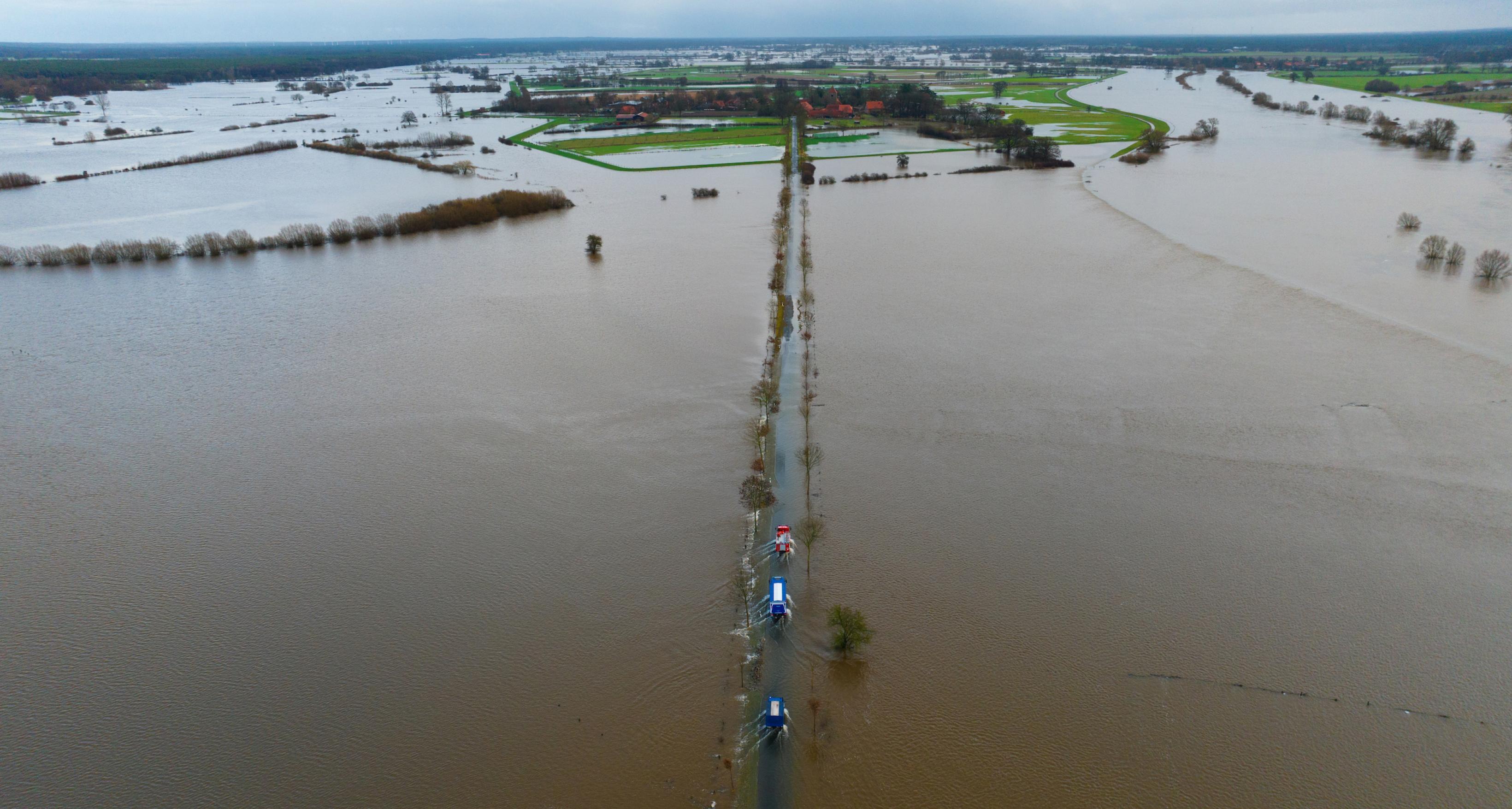 Ein Fahrzeug vom THW sowie der Feuerwehr fahren auf einer teilweise überfluteten Straße unweit der Aller (Aufnahme mit einer Drohne). Die Hochwasserlage bleibt in vielen Regionen Niedersachsens angespannt.