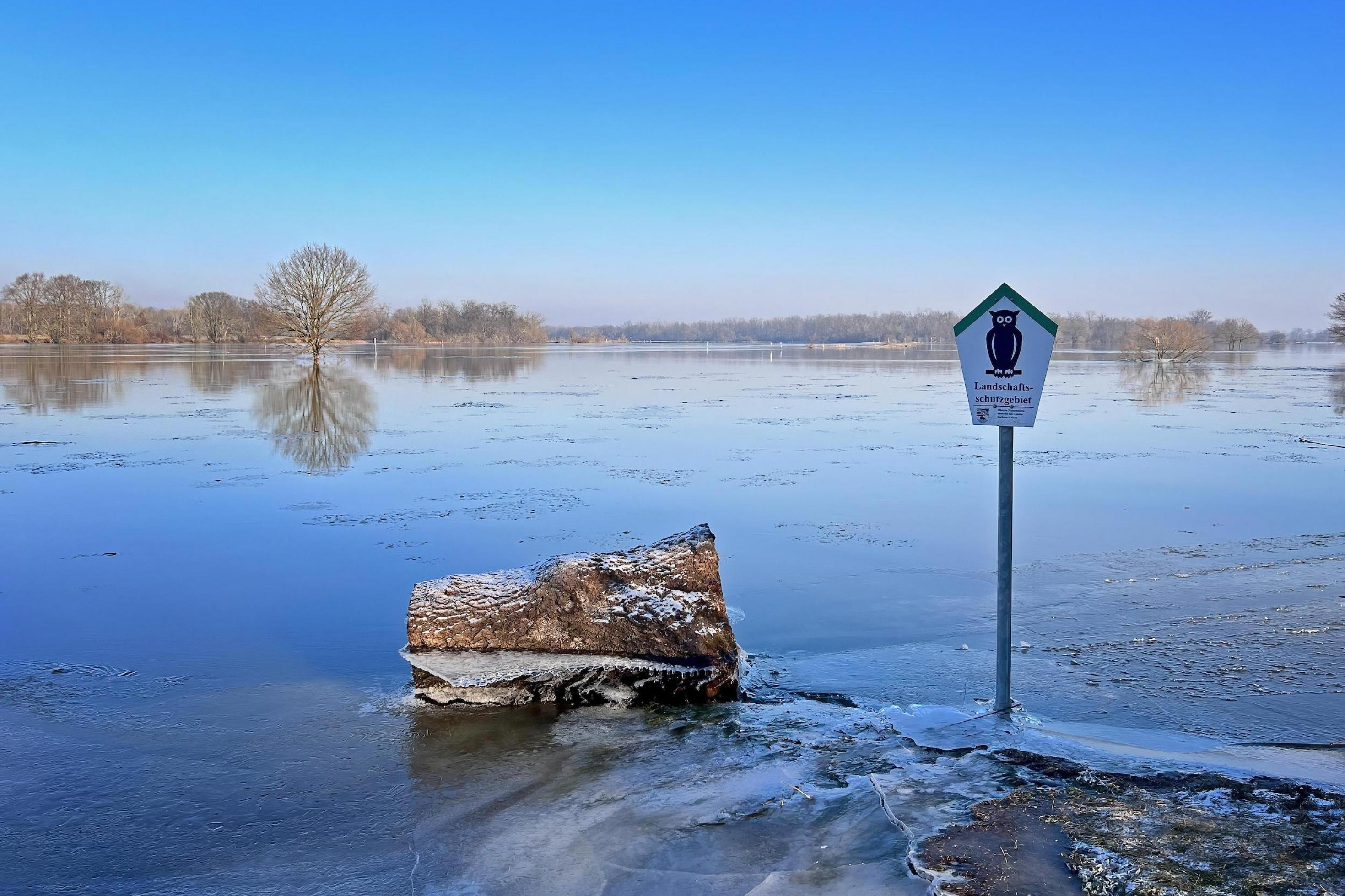 Große überfrorene Fläche in der Flusslandschaft, im Vordergrund ein Schild „Landschaftsschutzgebiet“