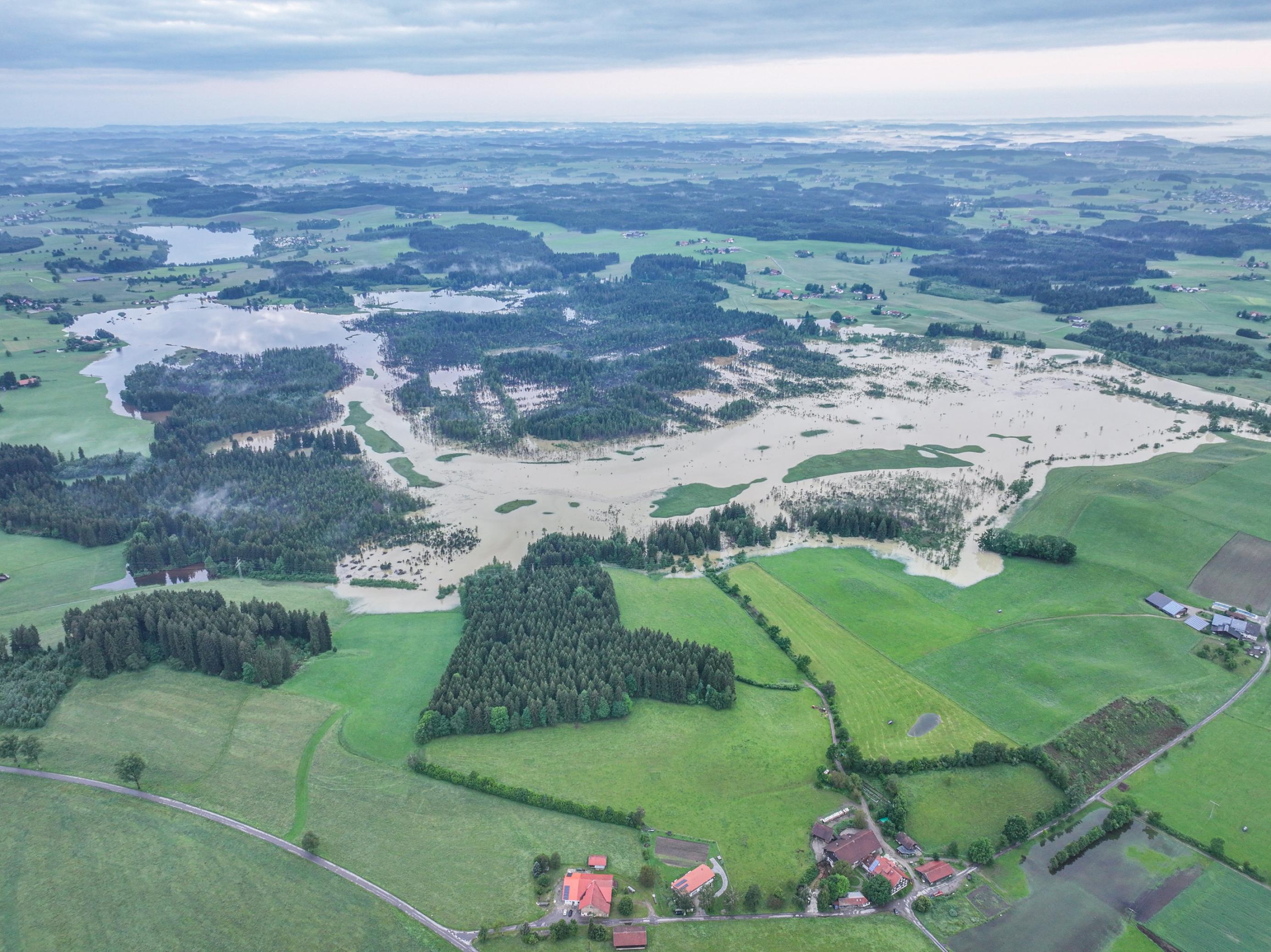 Luftbild einer Landschaft mit Wald, Grünland und Dörfern, in der unbesiedelte Gebiete überschwemmt sind.