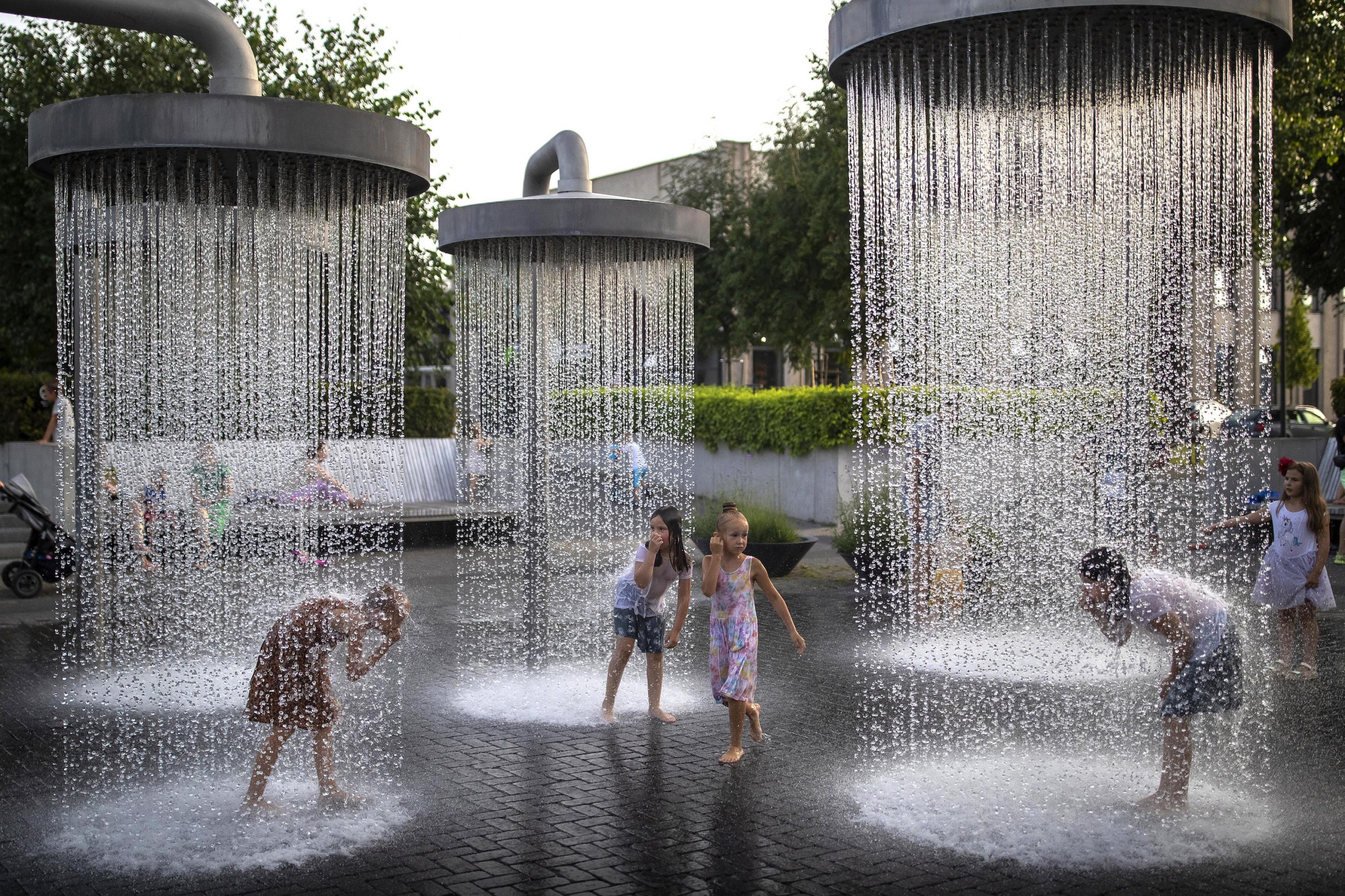 Kinder spielen unter riesigen Duschen, die im Stadtraum von Vilnius installiert sind.