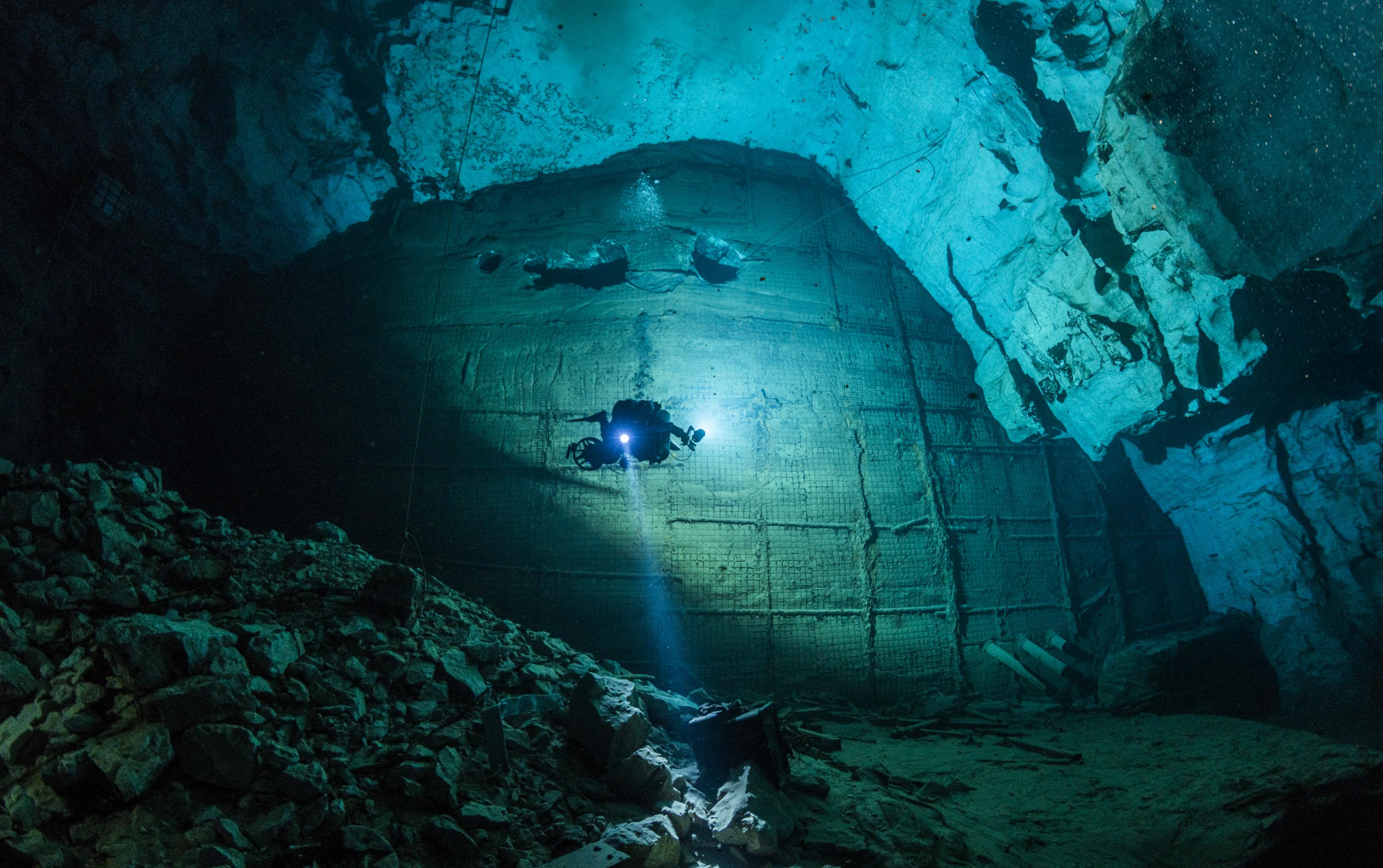 Taucher in einer Höhle, die mit einer großen Betonwand verschlossen ist