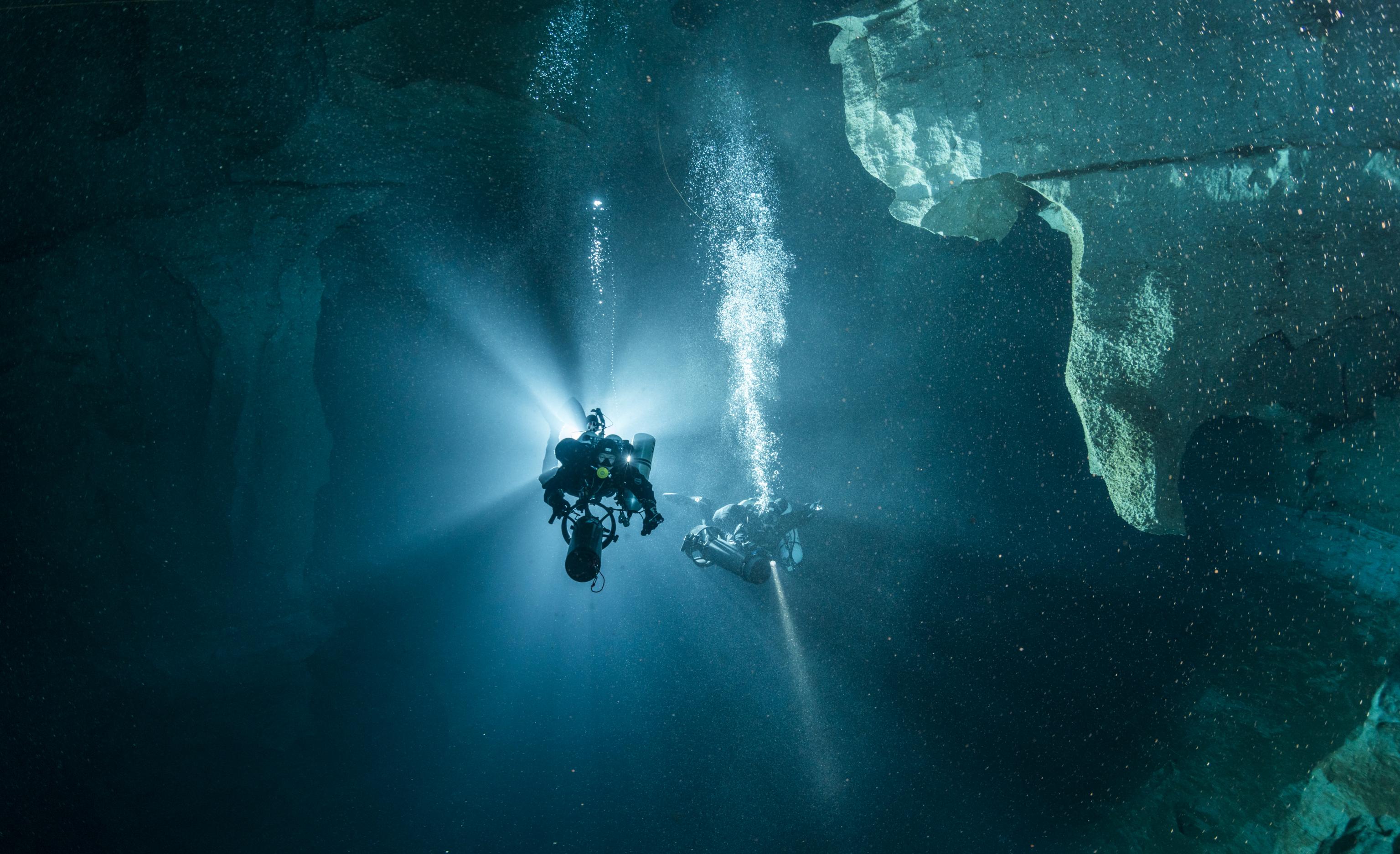 Taucher mit heller Taschenlampe in dunkler Höhle