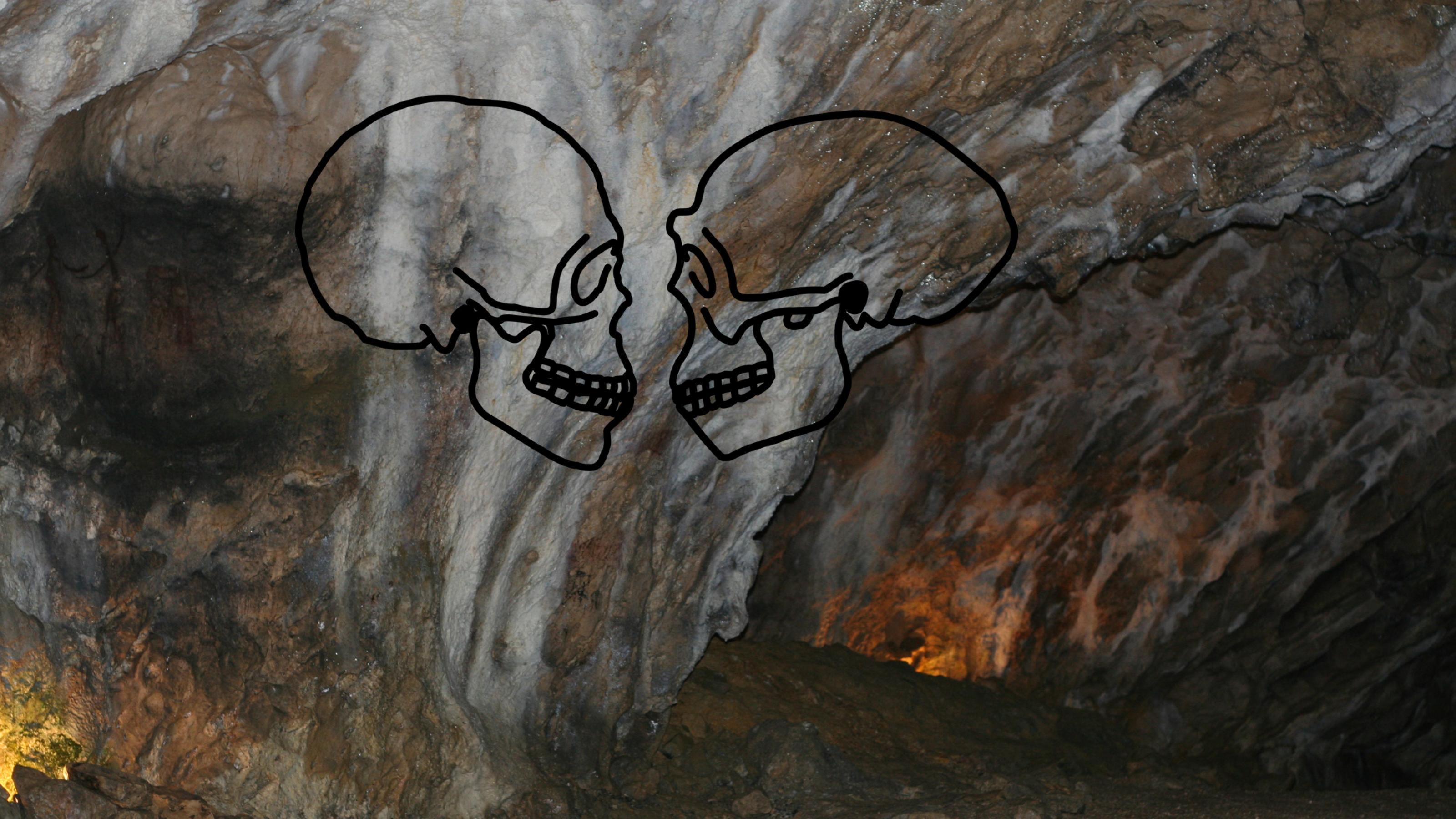 Blick auf die geheimnisvoll leuchtende Wand der Hohle Fels-Höhle in der Schwäbischen Alb. Hier fanden einst frühe Vertreter des Homo sapiens, aber auch andere Urmenschen ein Zuhause. Auf die Felswand projiziert sind die Schädelumrisse eines Homo sapiens und eines Homo erectus, die sich gegenseitig anschauen.