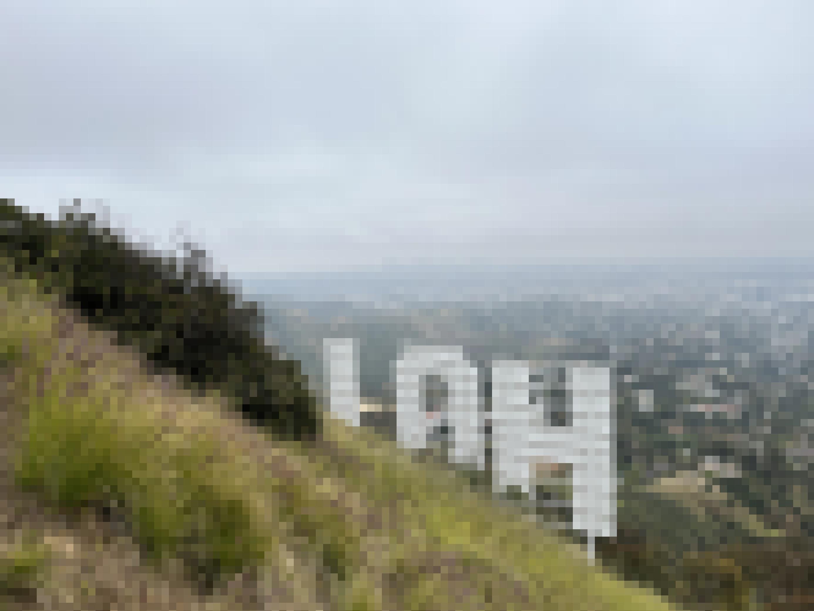 Das Hollywoodzeichen von hinten an einem steilen Hügel in diesigem Wetter. Nur die ersten drei Buchstaben – H, O, und L sind sichtbar.