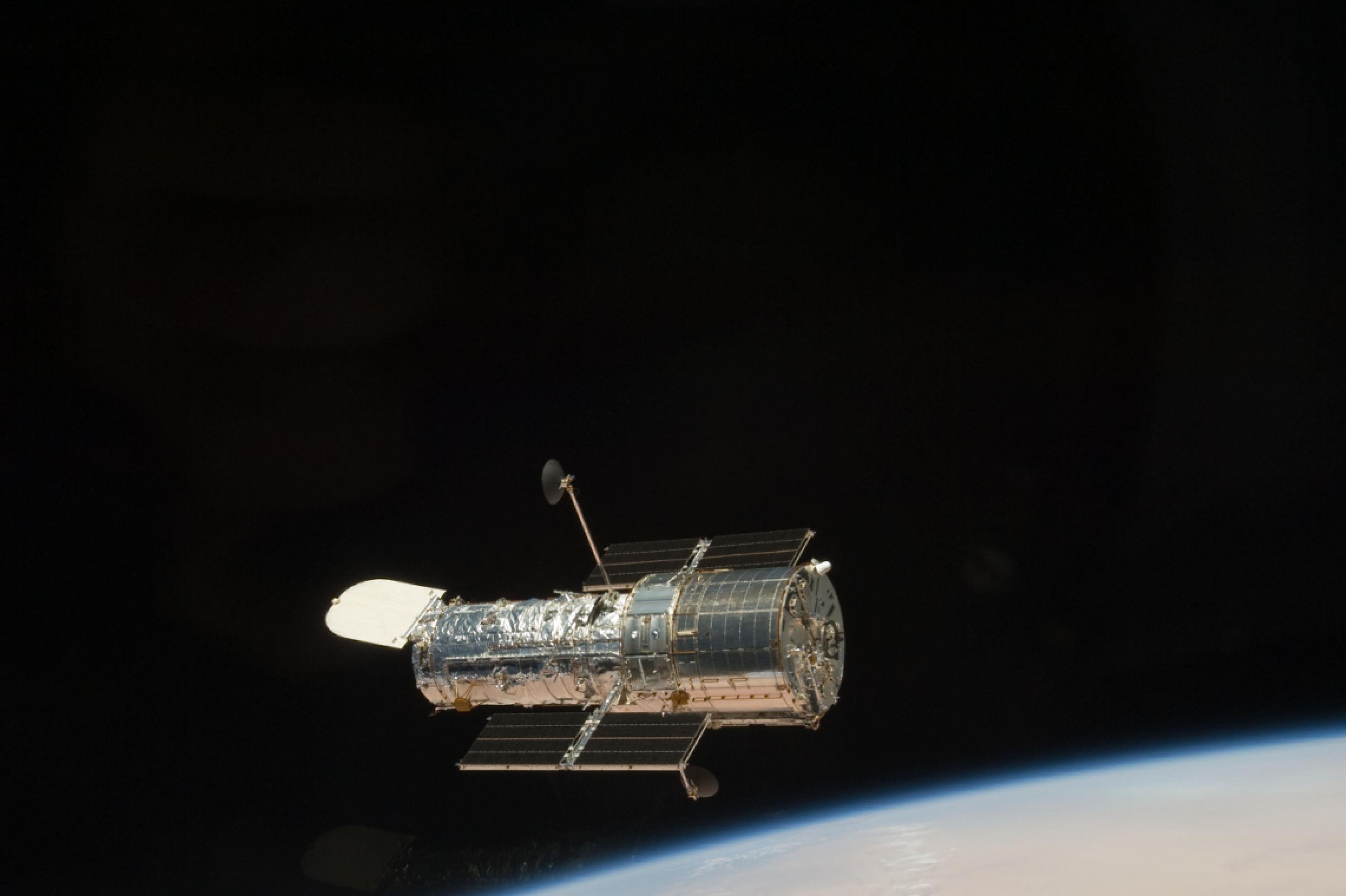 Das Hubble-Teleskop kreist über der Erde, die rötlich schimmert, was sich auf der metallischen Oberfläche des Teleskops widerspiegelt.