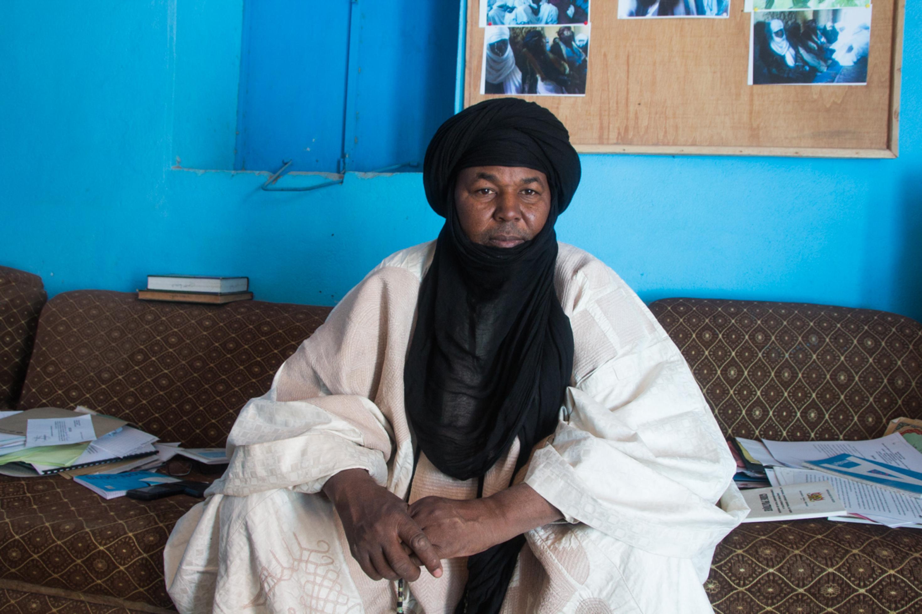 Imam Liman Ahar Fidjaji trägt ein schwarzes Tuch um Kopf und Hals. Er sitzt auf einem Sofa.