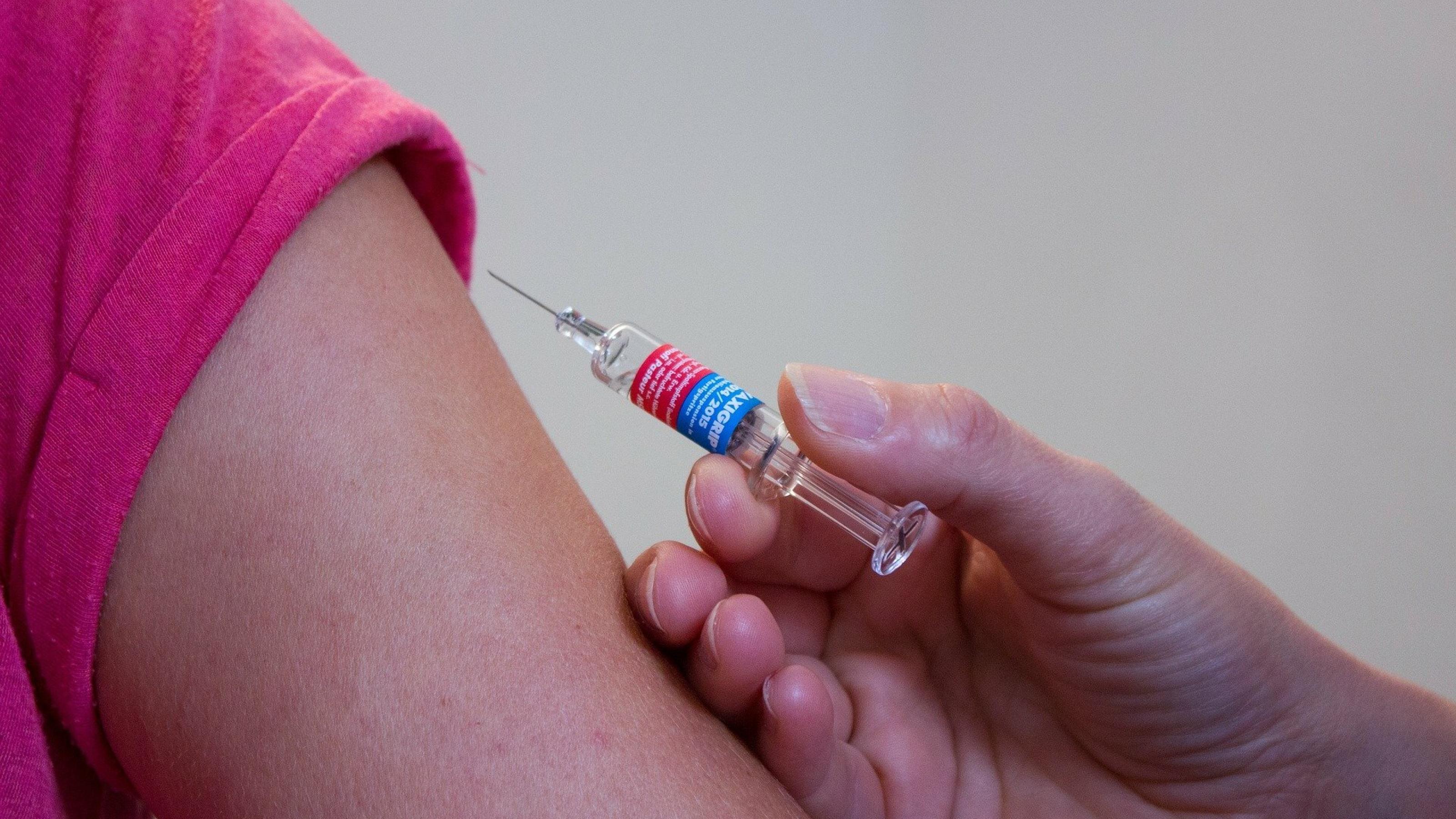 Eine Hand mit einer Impfstoff-Spritze kurz vor der Infektion in den Muskel in den Oberarm eines Menschen.