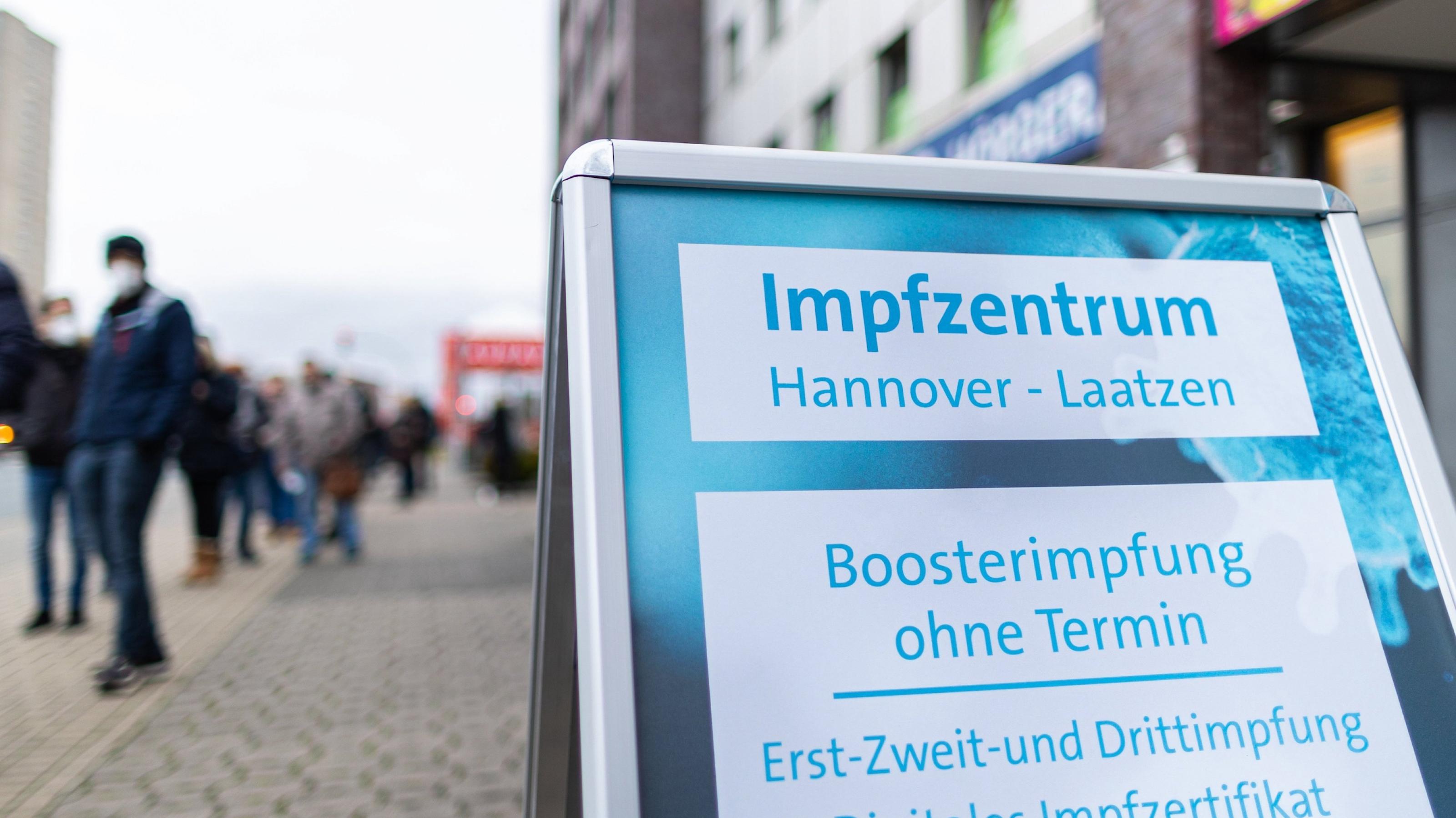 Menschen warten in einer langen Schlange vor dem Eingang zum Impfzentrum. Auf dem Schild werden Boosterimpfungen ohne Termin in Hannover angeboten.