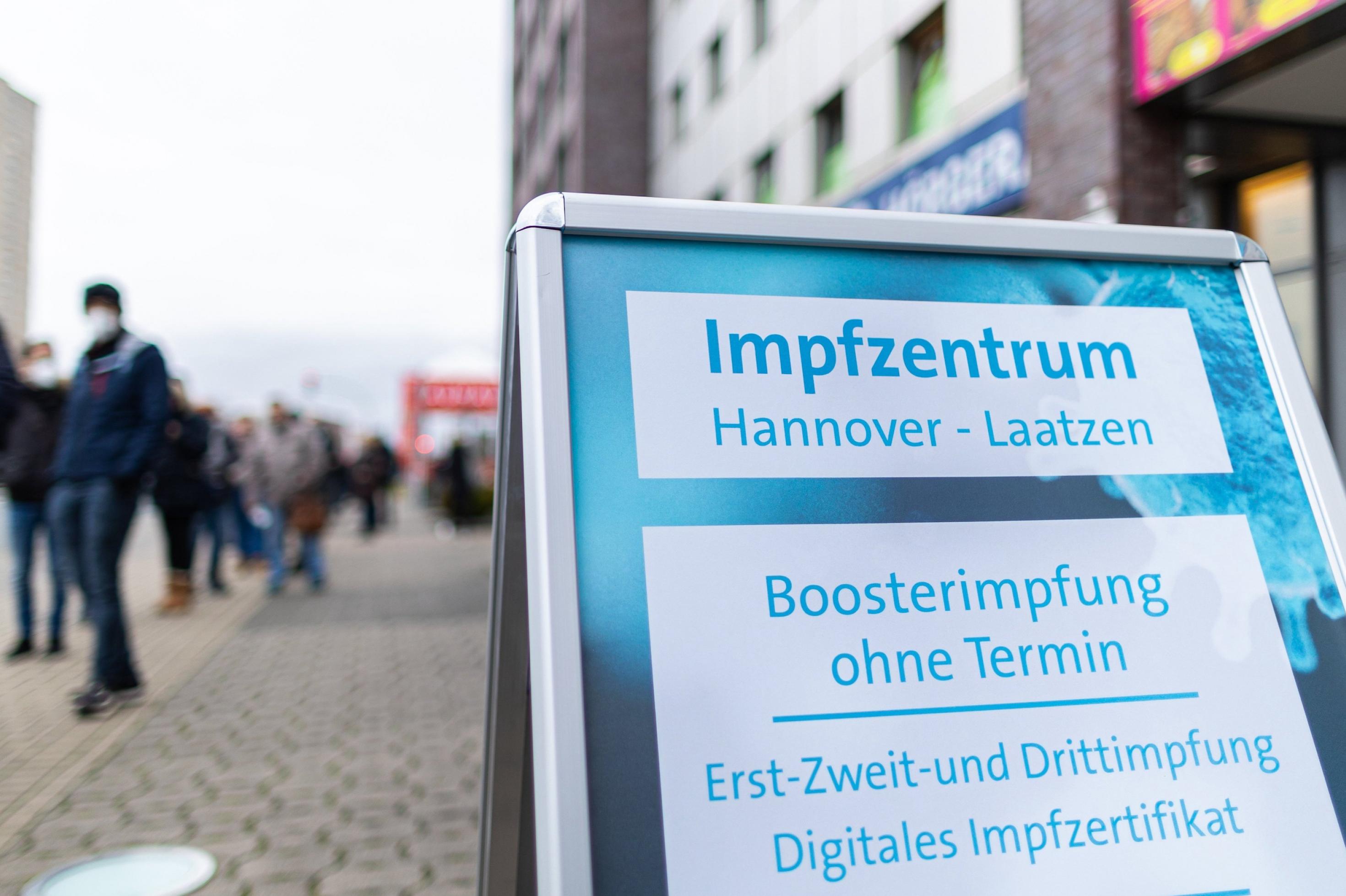 Menschen warten in einer langen Schlange vor dem Eingang zum Impfzentrum. Auf dem Schild werden Boosterimpfungen ohne Termin in Hannover angeboten.