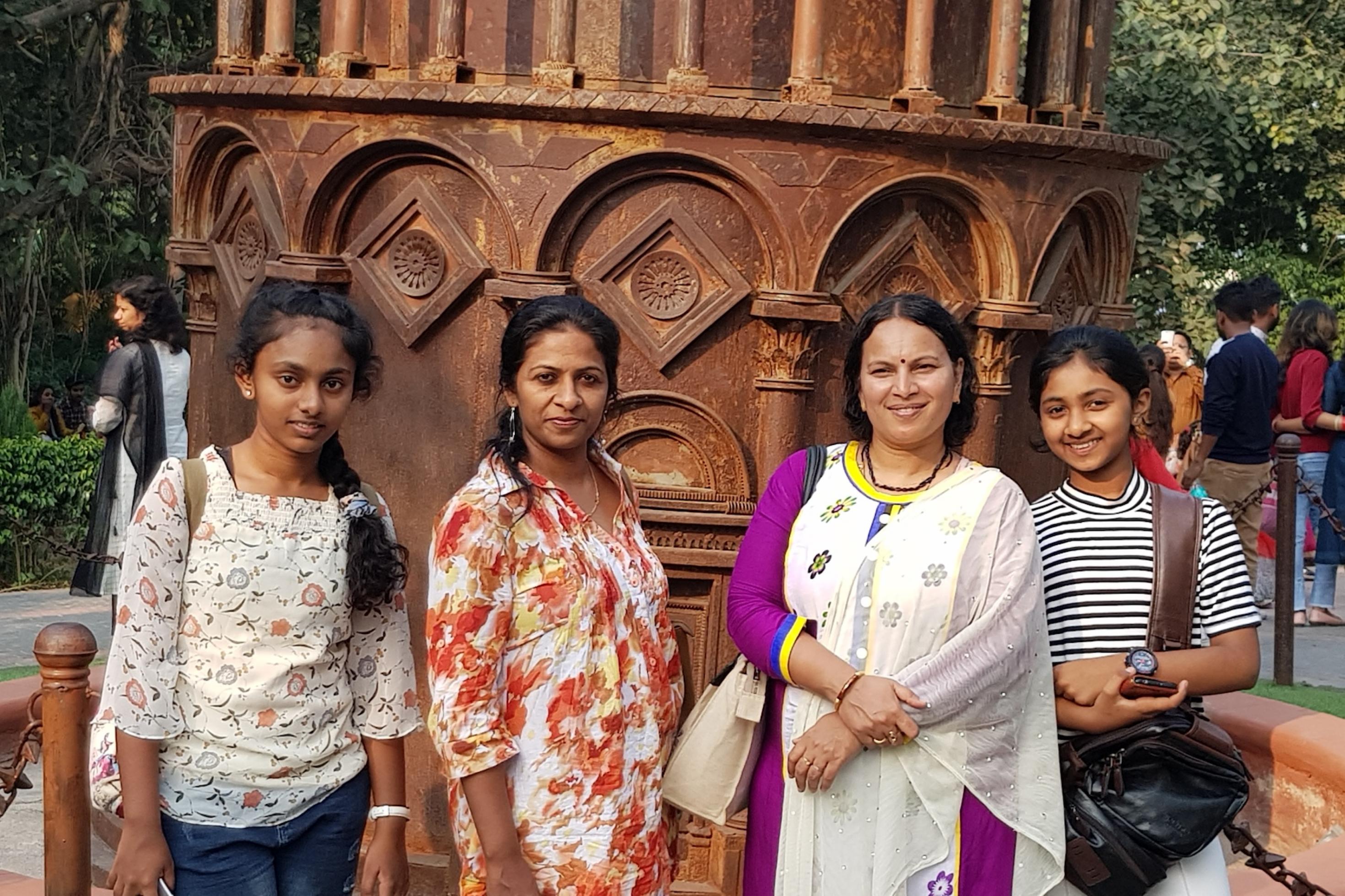 Vier Frauen verschiedenen Alters stehen vor einem Bauwerk oder Denkmal. Zwei von ihnen sind mit T-Shirt oder Bluse eher international gekleidet, zwei eher indisch oder traditionell. Alle blicken selbstbewusst und lächelnd in die Kamera.