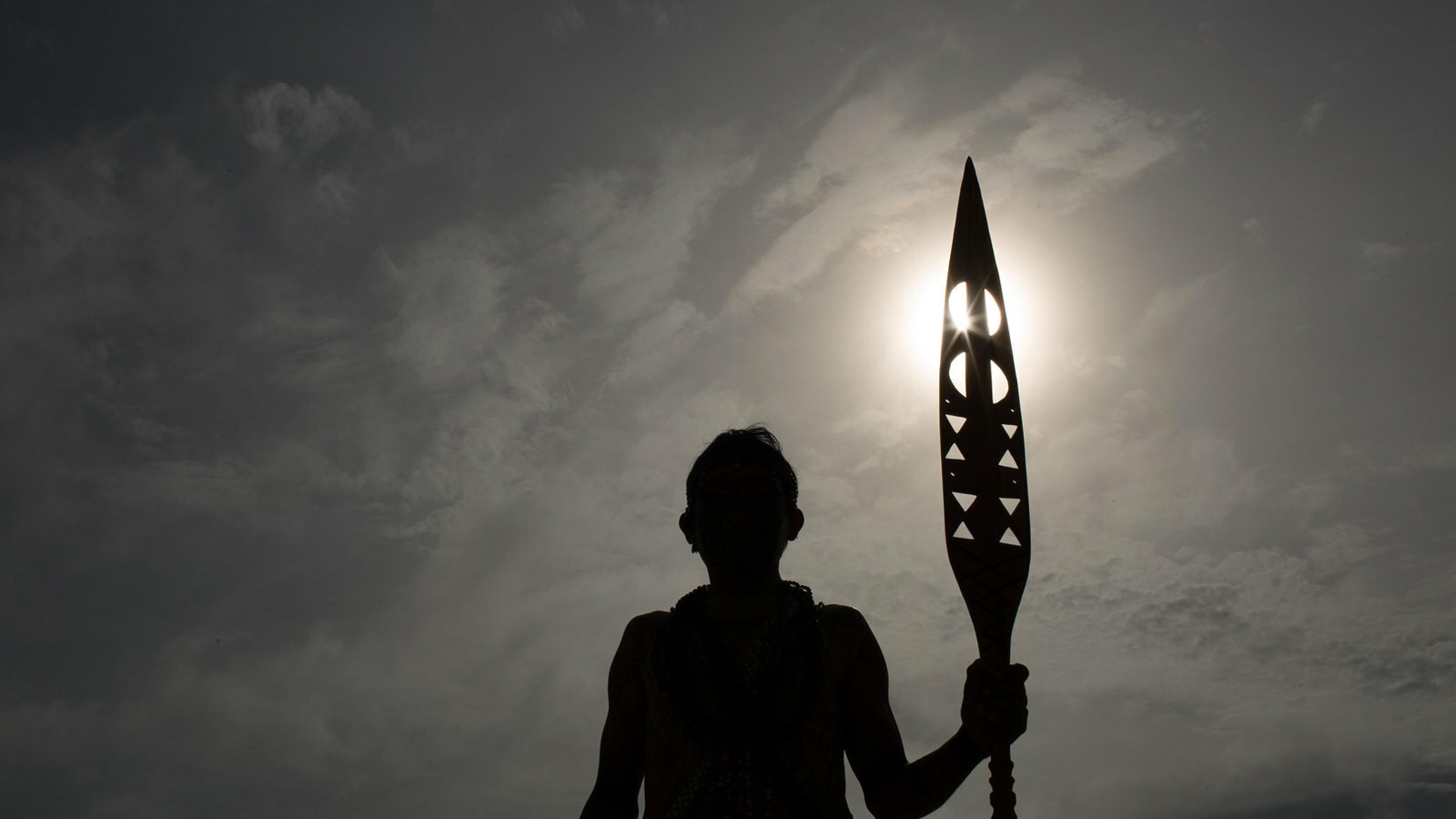 Gegenlichtaufnahme eines Indigenen mit einem geschnitzten Zeremonialstab.