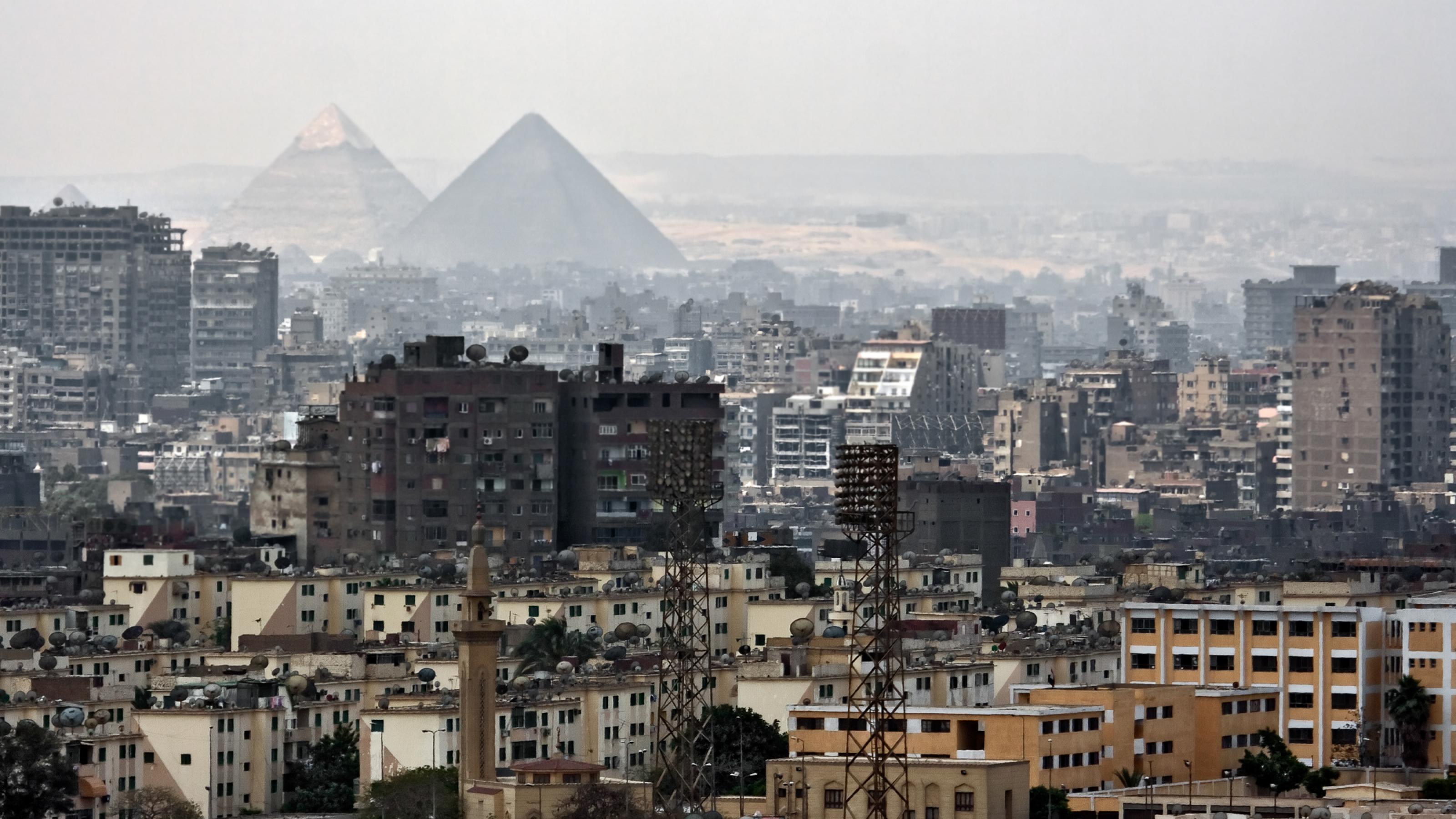Das Symbolbild zeigt die Skyline von Kairo – im Vordergrund Wohnblocks, im Hintergrund Pyramiden.