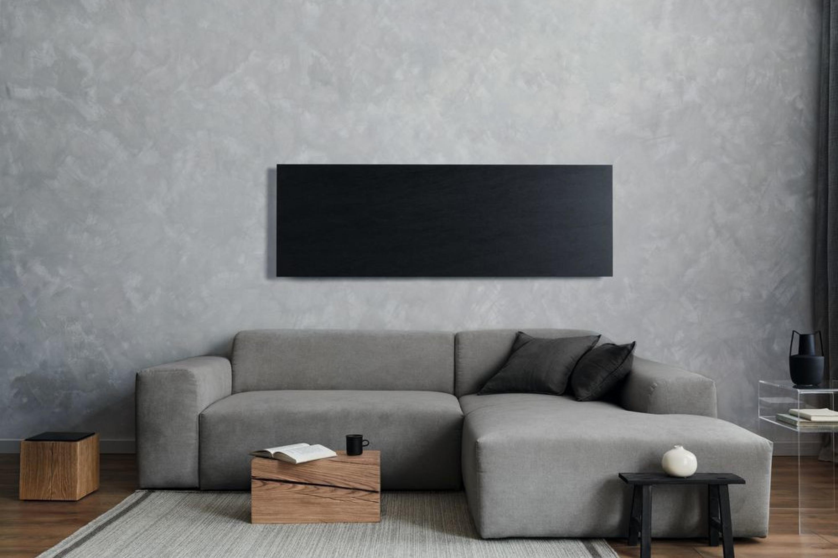 Schwarze Infrarot-Heizplatte, die über einem grauen Sofa an einer grauen Wand installiert ist