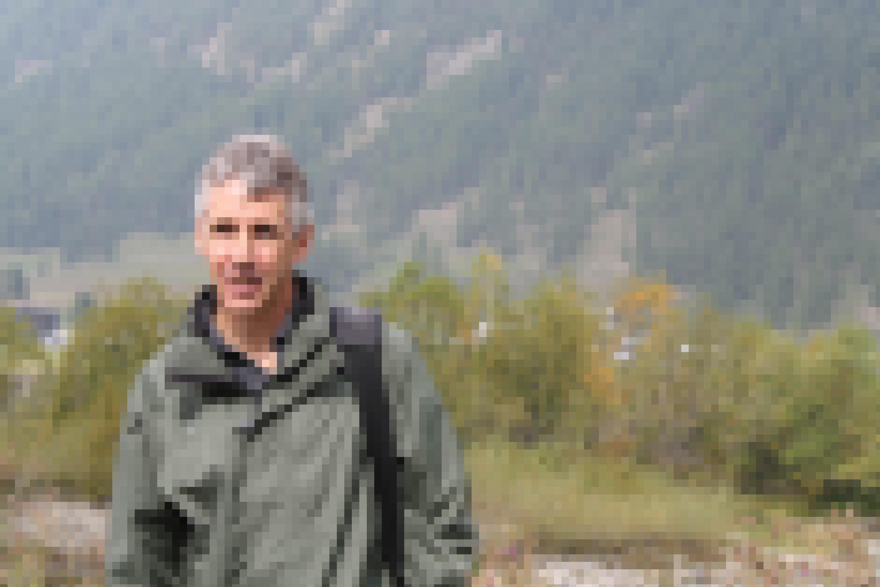 grauhaariger schlanker Mann steht in Alpen-Flusslandschaft