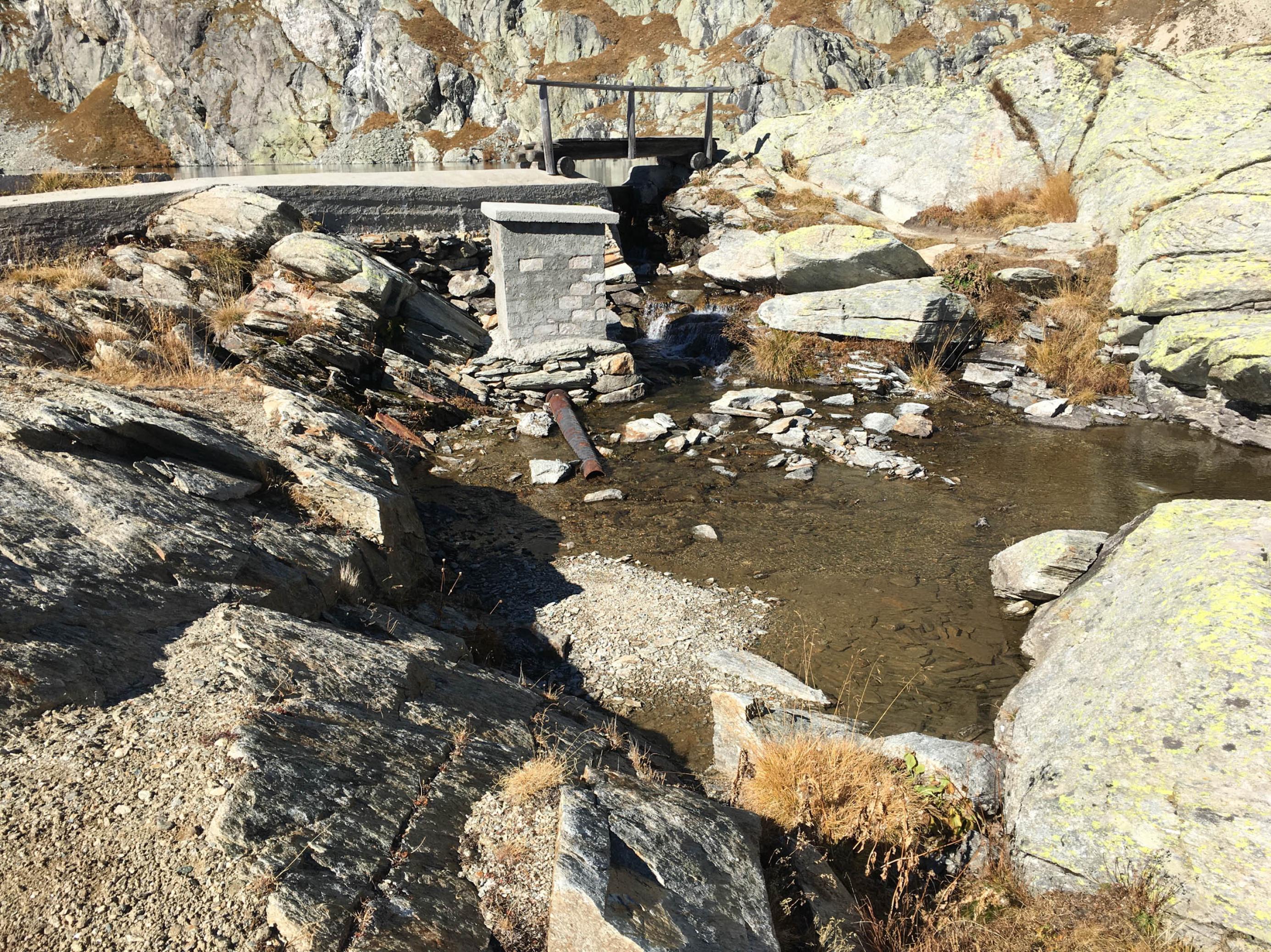 Bergsee mit kleiner Betonmauer und Metallrohr