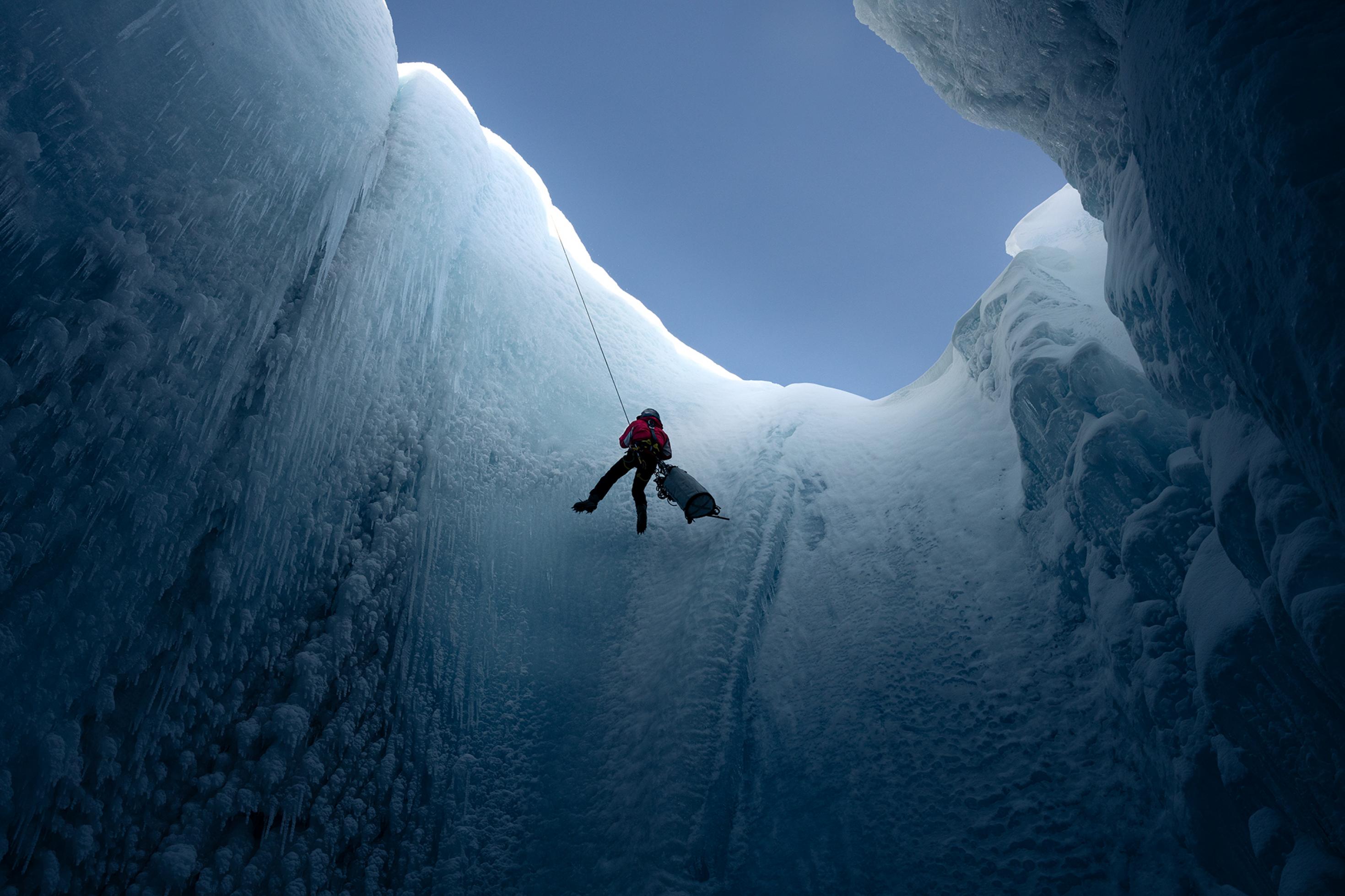 Aus der Tiefe einer Gletschermühle aufgenommen sieht man den Glaziologen Alun Hubbard am Seil hängend. Er ist gerade dabei, sich in das Eisloch im Gletscher abzuseilen.