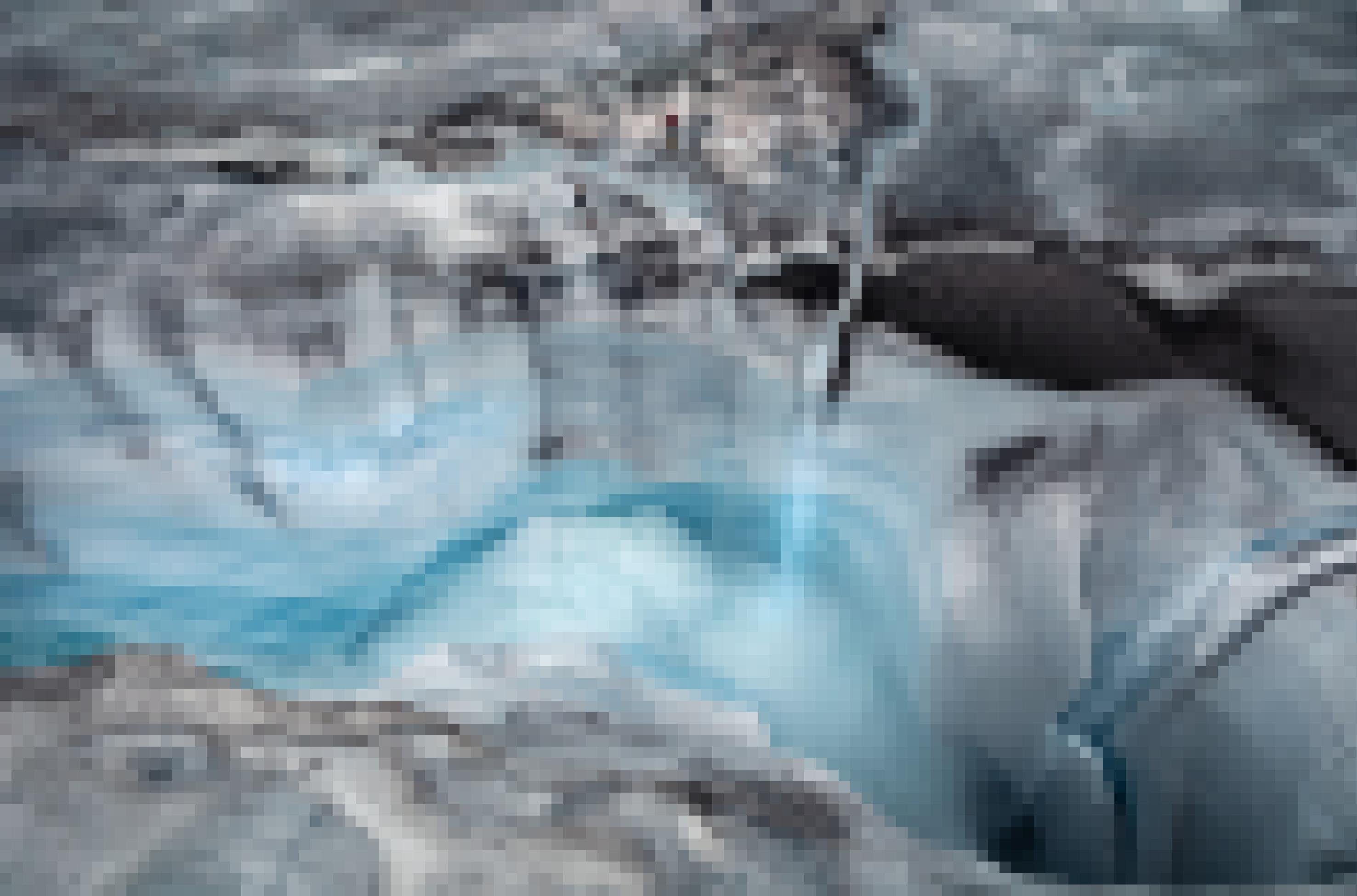Der Forscher Alun Hubbard und der Regisseur Lars Ostenfeld sind in diesr Luftaufnahme als kleine Figuren am Rand einer Gletschermühle zu sehen. Sie haben sich mit Seilen gesichert und werfen einen ersten Blick in das tiefe Loch im grönländischen Eis.