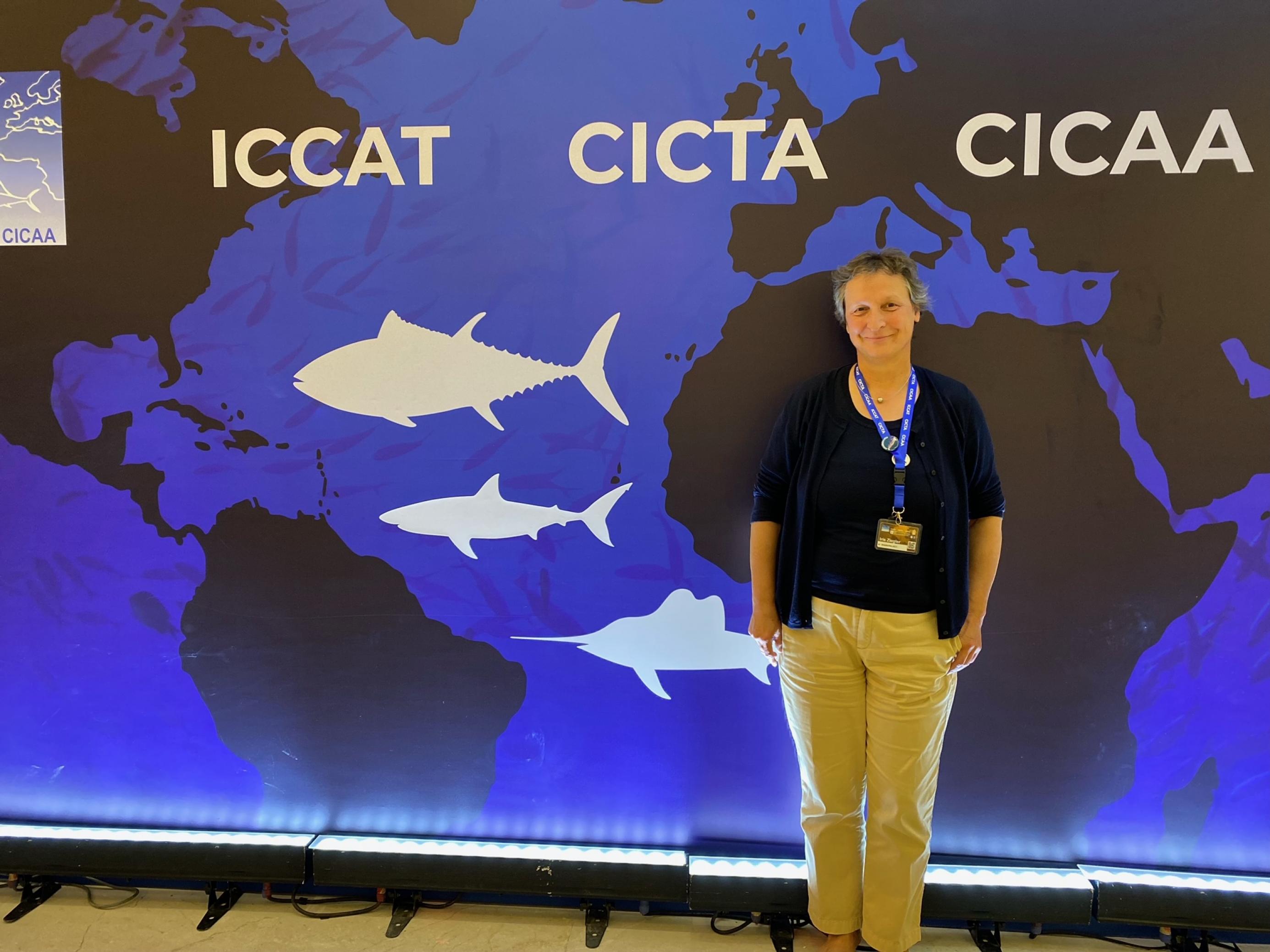 Iris Ziegler steht vor einer Wand mit dem Logo von ICCAT. Sie trägt eine helle Hose.