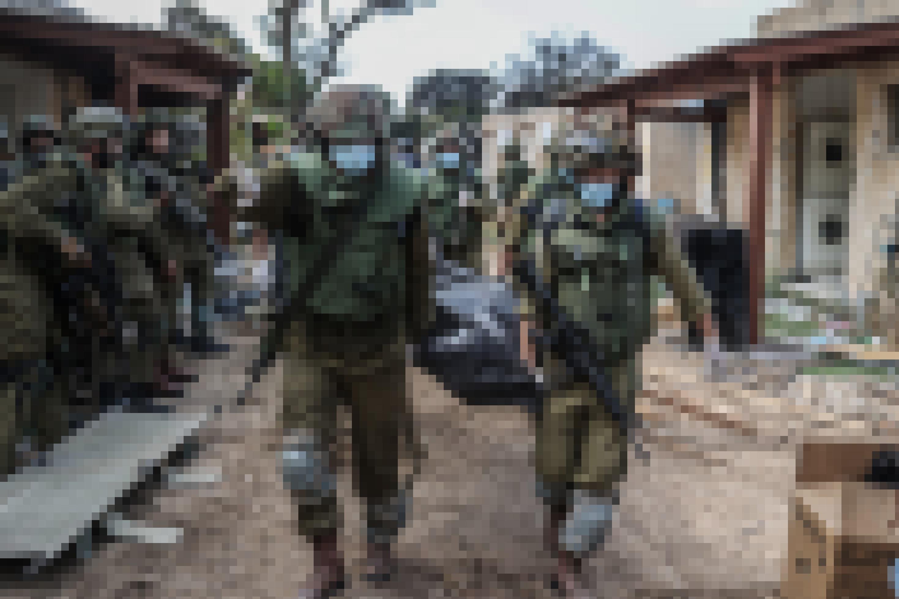 Soldaten mit umgehängten Gewehren tragen Baren mit in Leichensäcken verhüllten Körpern