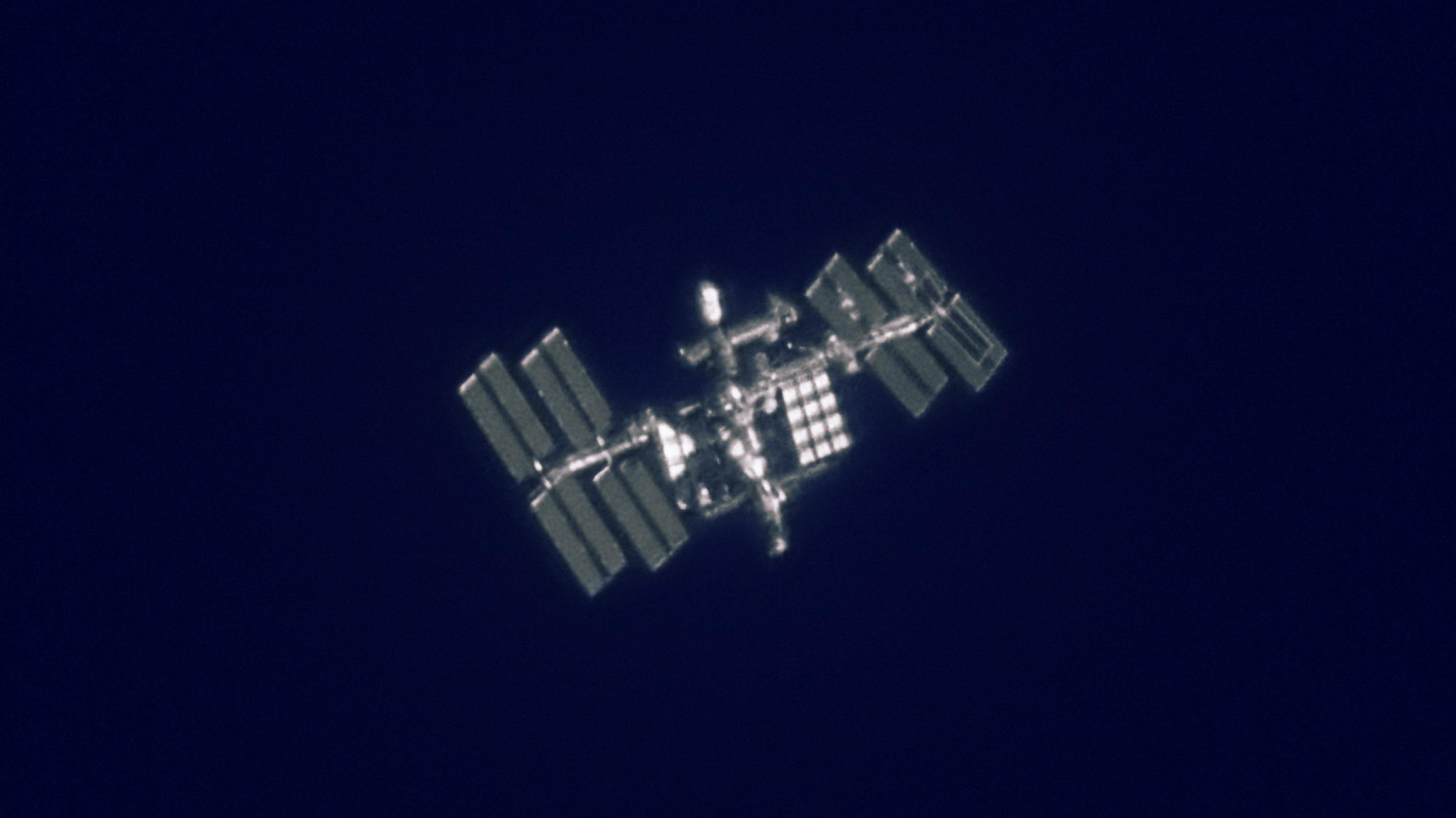Detailreiche Strukturen an der Internationalen Raumstation ISS wie Solarpaneele und Arbeitsmodule lassen sich auch von der Erde aus fotografieren; selbst zwei Astronauten bei einem Außenbordeinsatz sind zu erkennen.