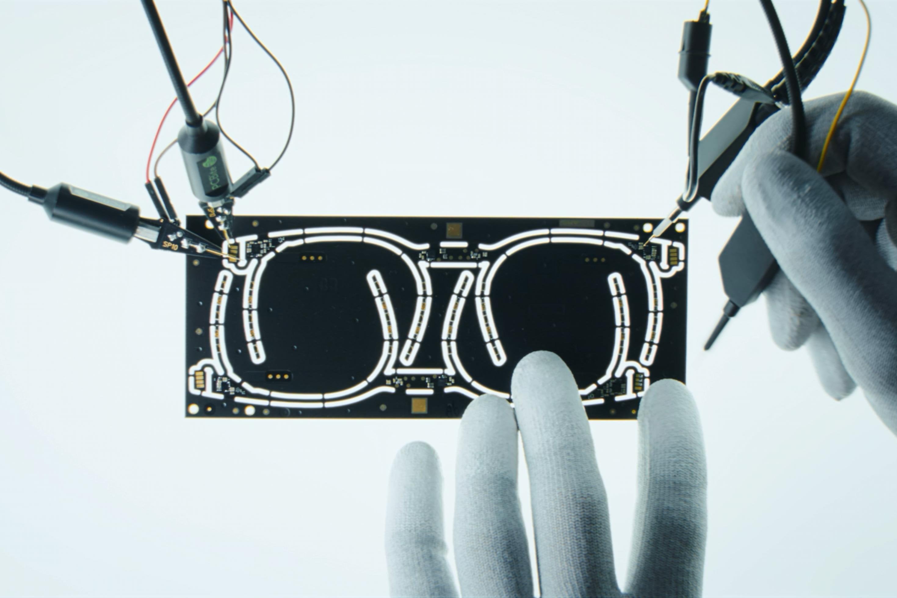 Zwei behandschuhte Hände arbeiten Schaltkreis einer smarten Brille im Frühstadium.