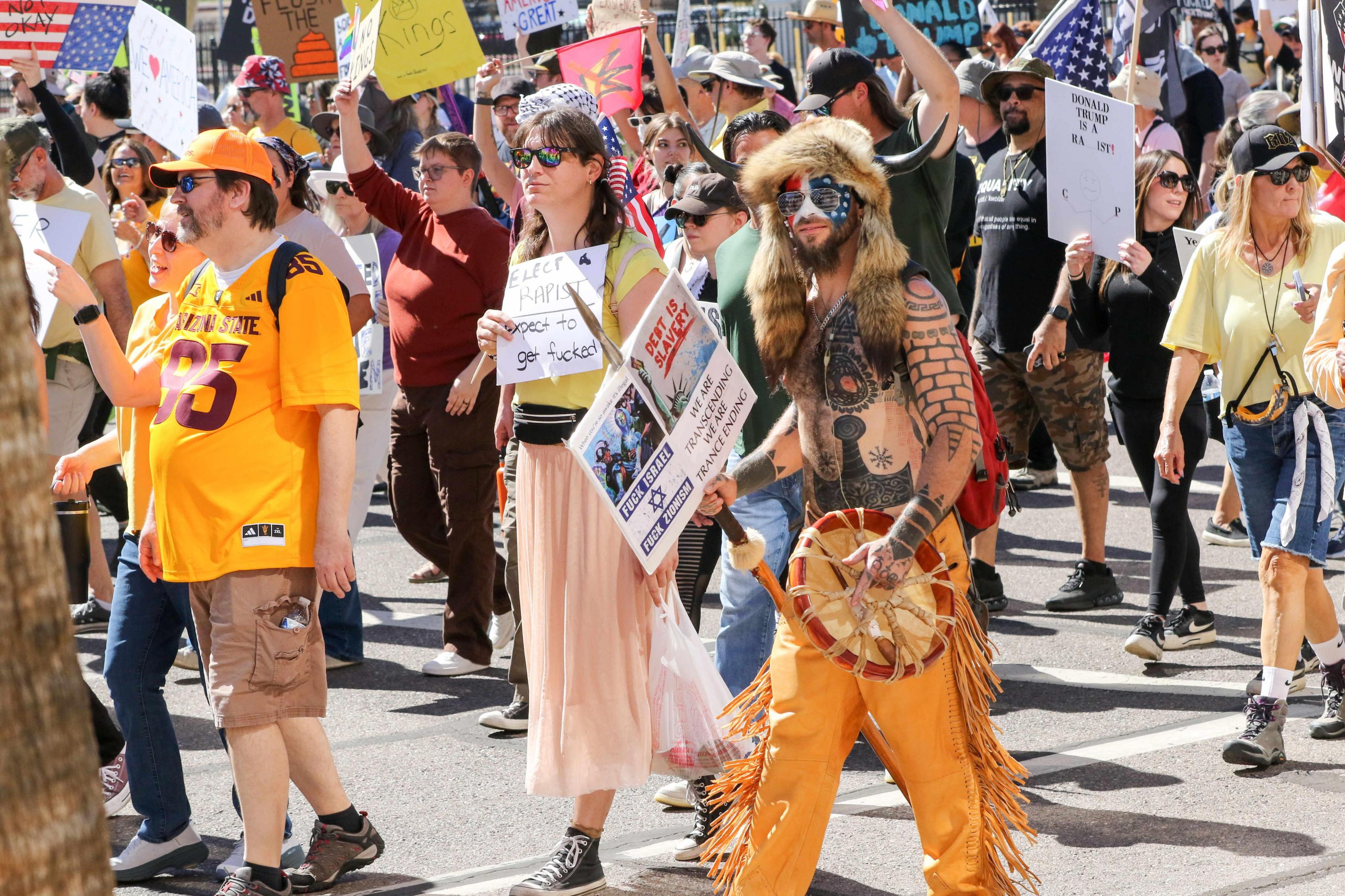 Jacob Angeli-Chansley, gekleidet mit Fellmütze, bemalt mit USA-Fahne, hält ein Plakat auf einer Demo in der Hand.