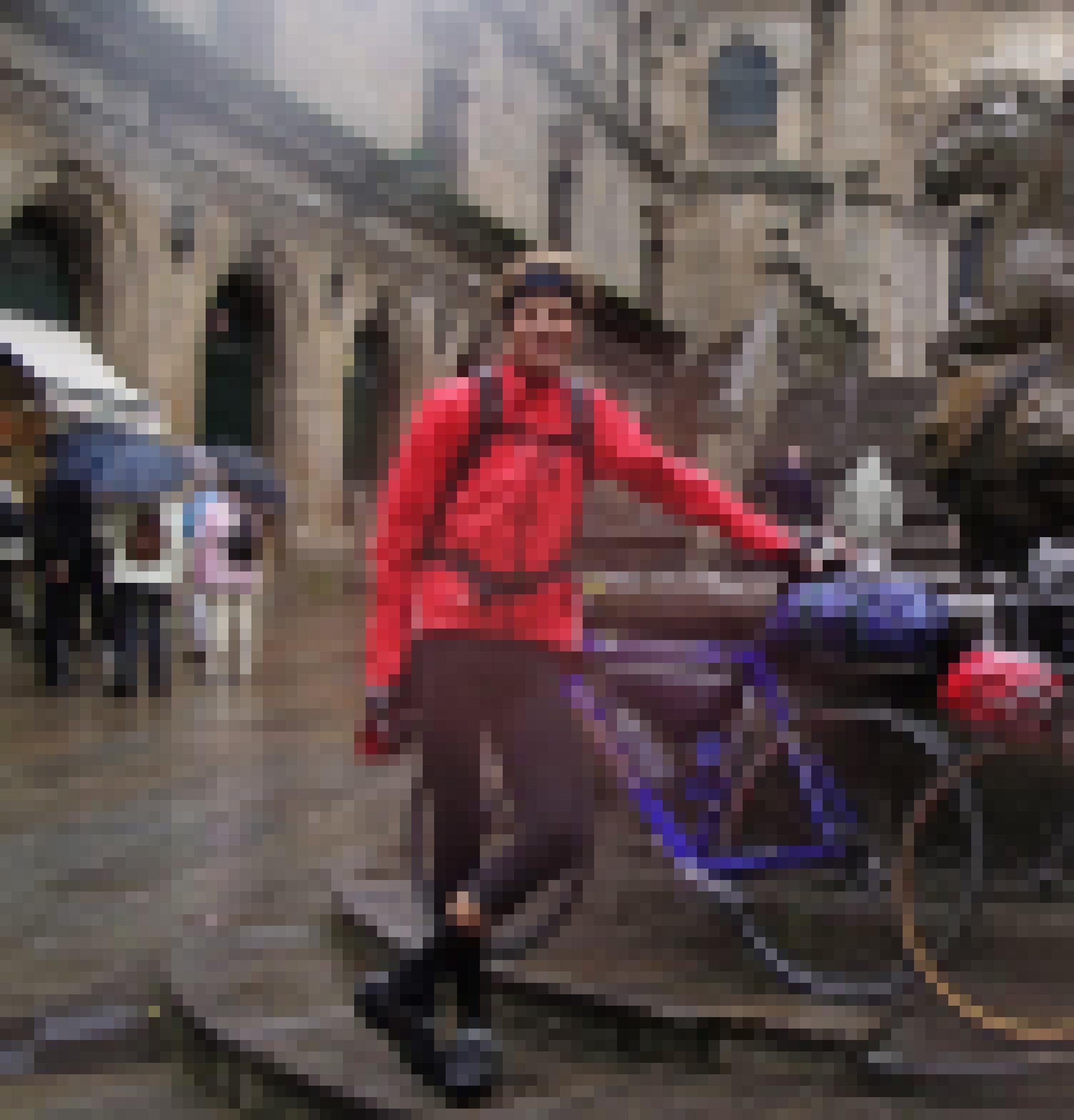Durchnässt, aber glücklich lächelnd steht der Autor in roter Regenjacke mit seinem blauen Rennrad vor einem steinernen Brunnen, neben dem Touristen mit aufgespannten Regenschirmen flanieren.