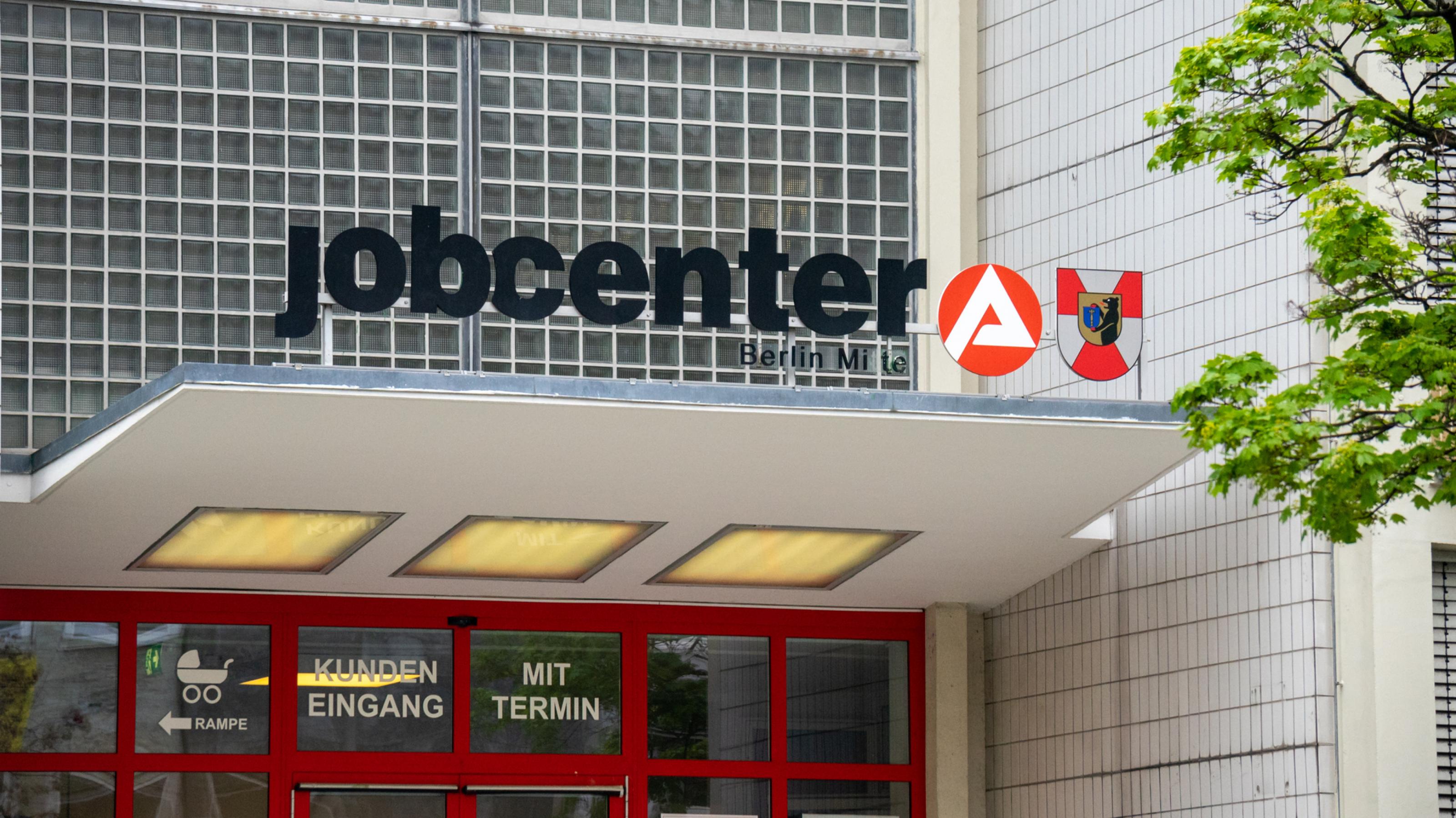 Eingang des Jobcenters in Berlin-Mitte mit dem großen Logo der Behörde auf einem Vordach.