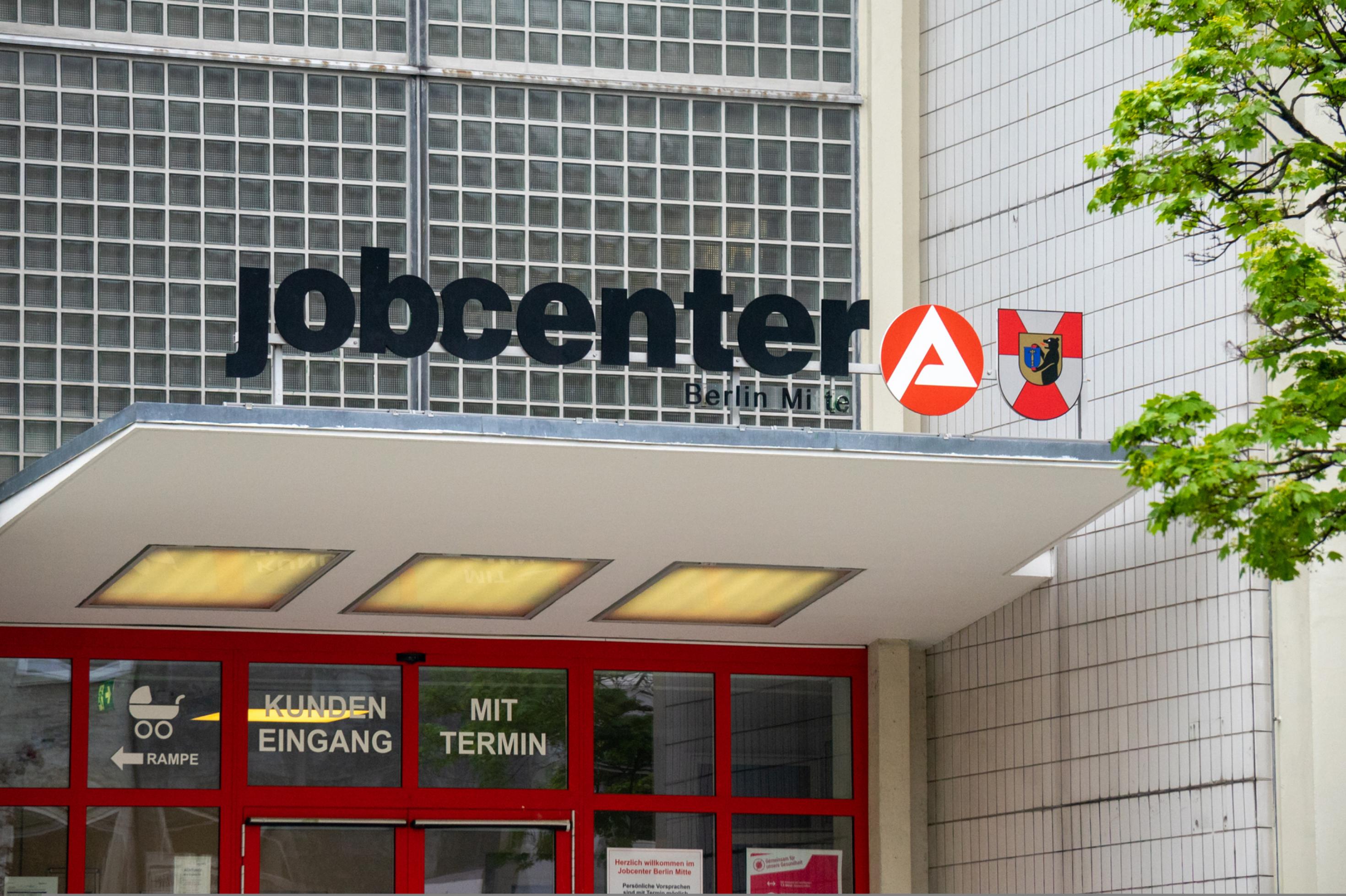 Eingang des Jobcenters in Berlin-Mitte mit dem großen Logo der Behörde auf einem Vordach.