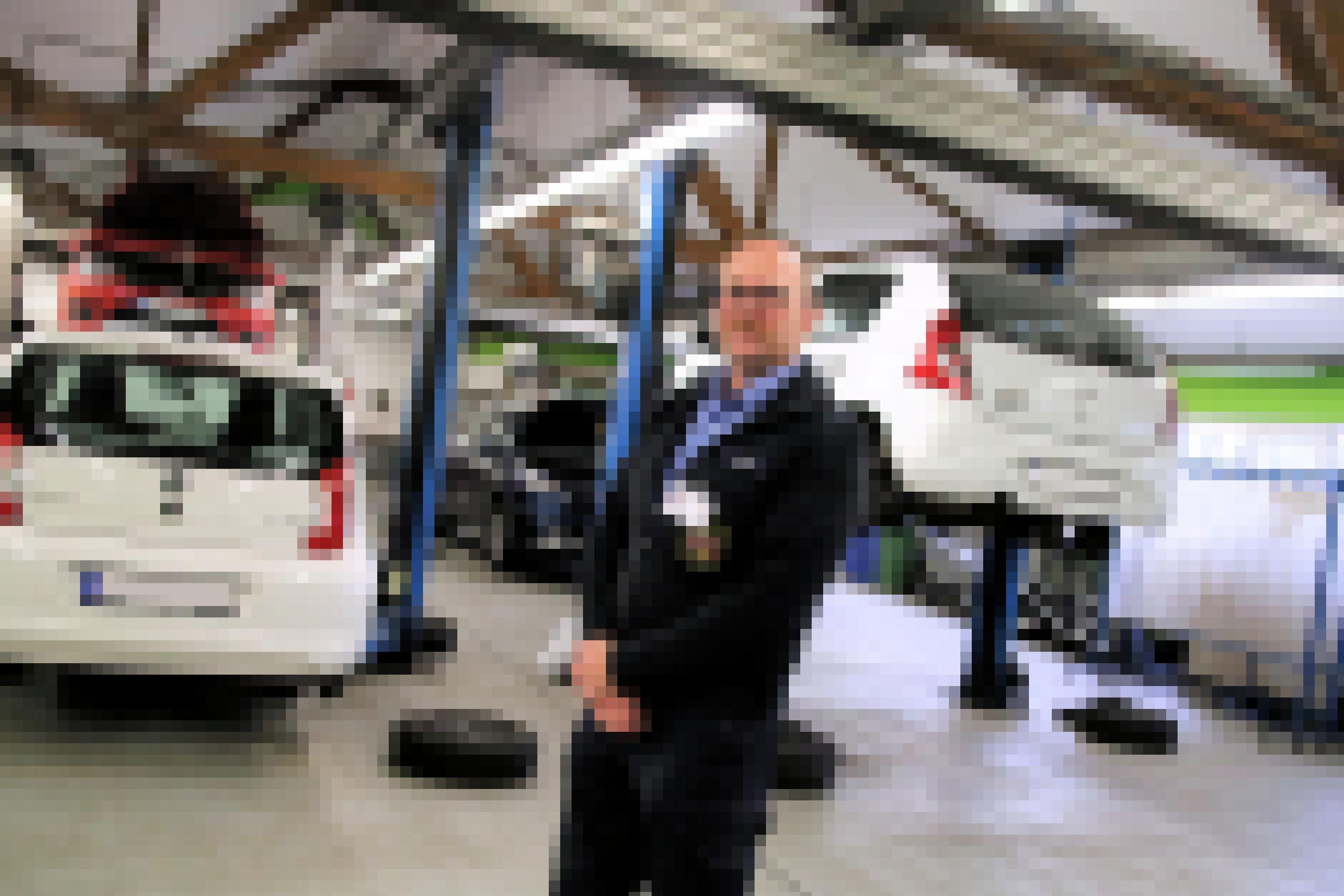 Uniformierter Mann steht zwischen Autos in Kfz-Werkstatt.