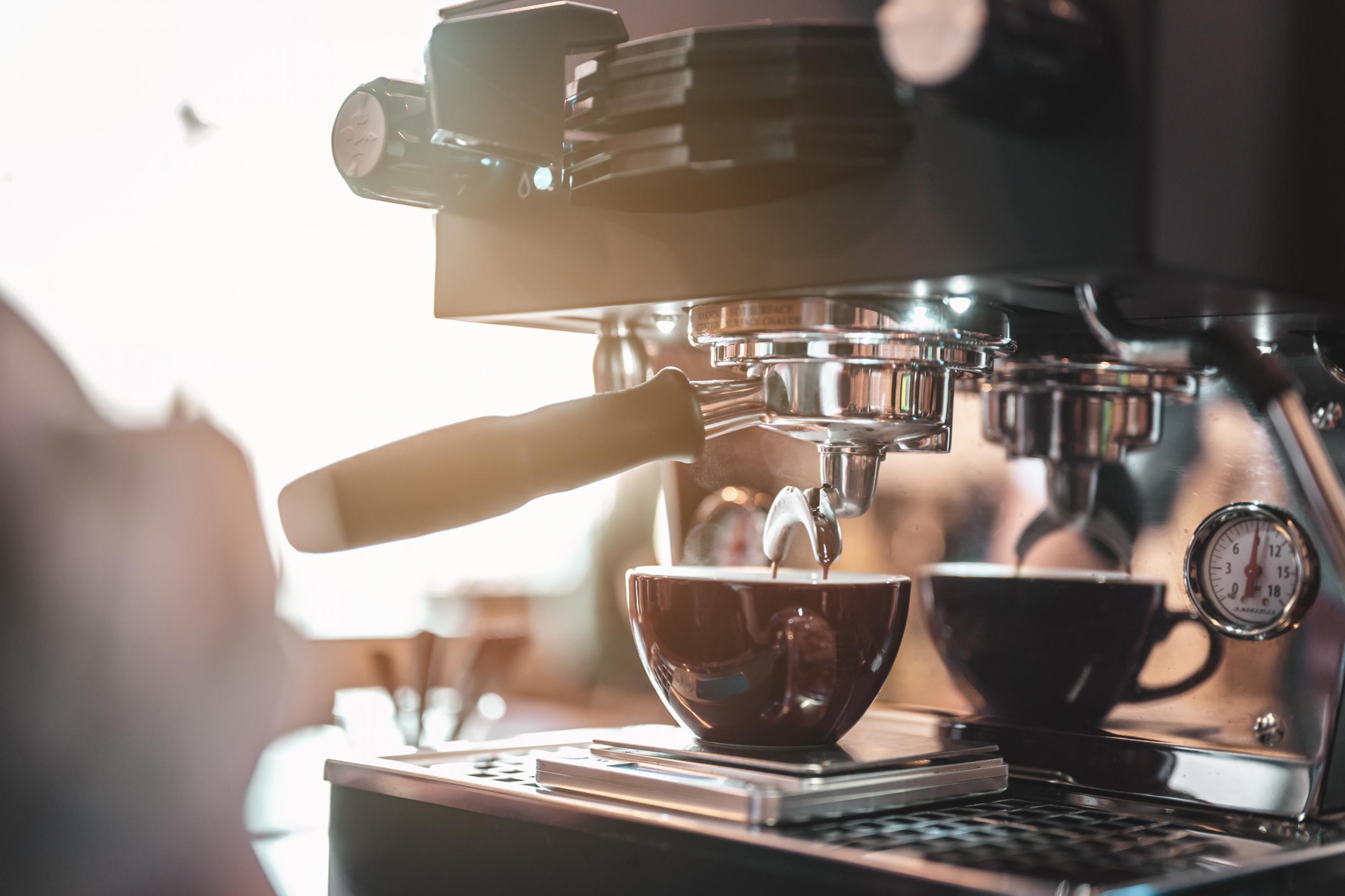 Nahaufnahme einer Kaffeemaschine mit einer Kaffeetasse – fotografiert mit etwas Gegenlicht.
