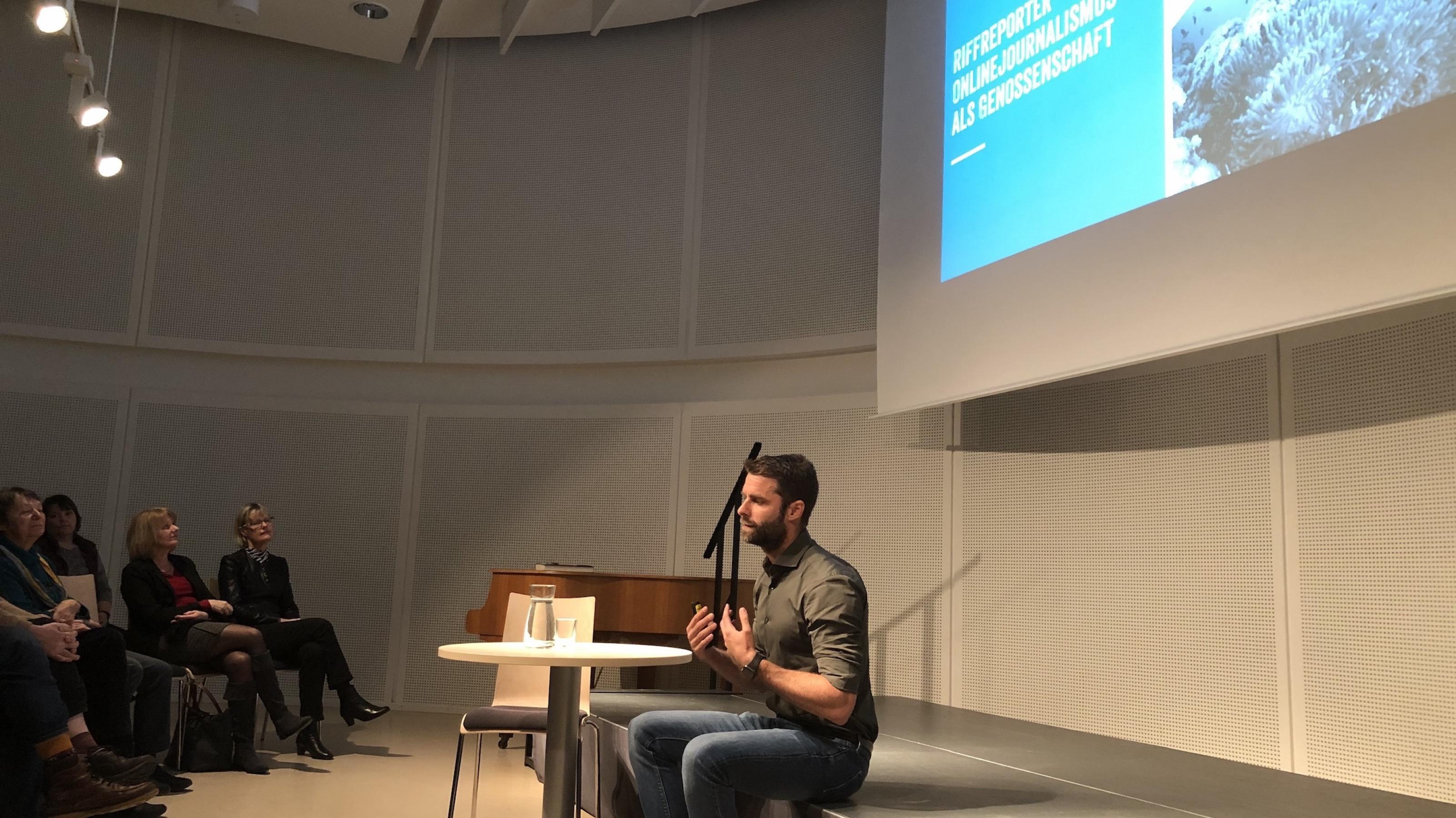 Der Journalist Kai Kupferschmidt sitzt auf einer Bühne und spricht, vor ihm das Publikum der Stadt- und Landesbibliothek Potsdam.