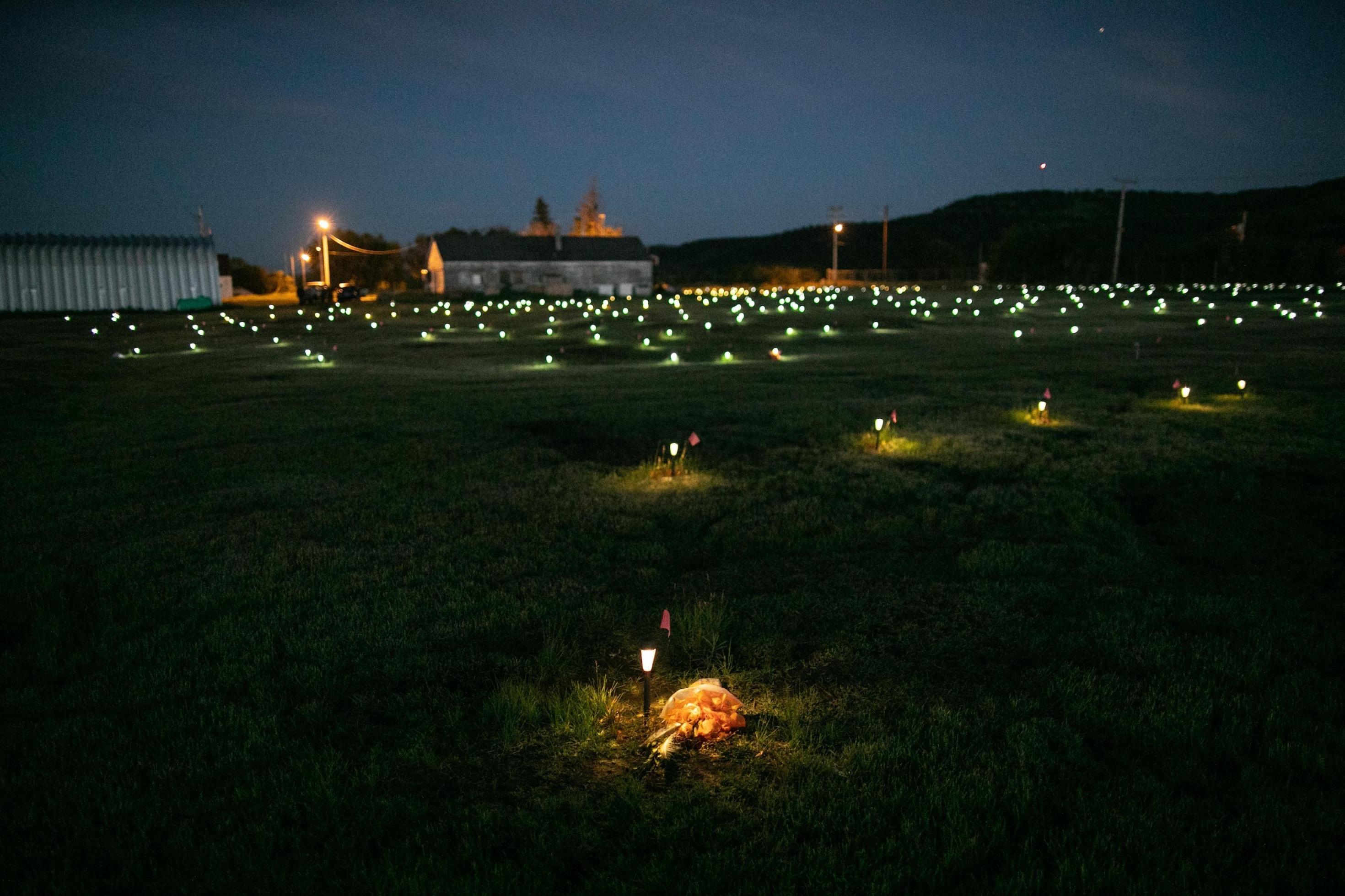 In der Dämmerung leuchten zahlreiche Solarlämpchen auf der Wiese vor einer Kirche, sie markieren die aufgefundenen Kindergräber.